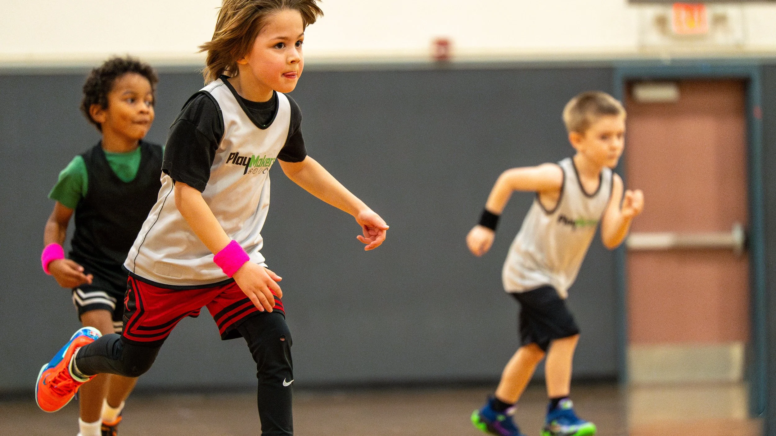 Children running indoors during a sports activity, wearing athletic clothing and sneakers.