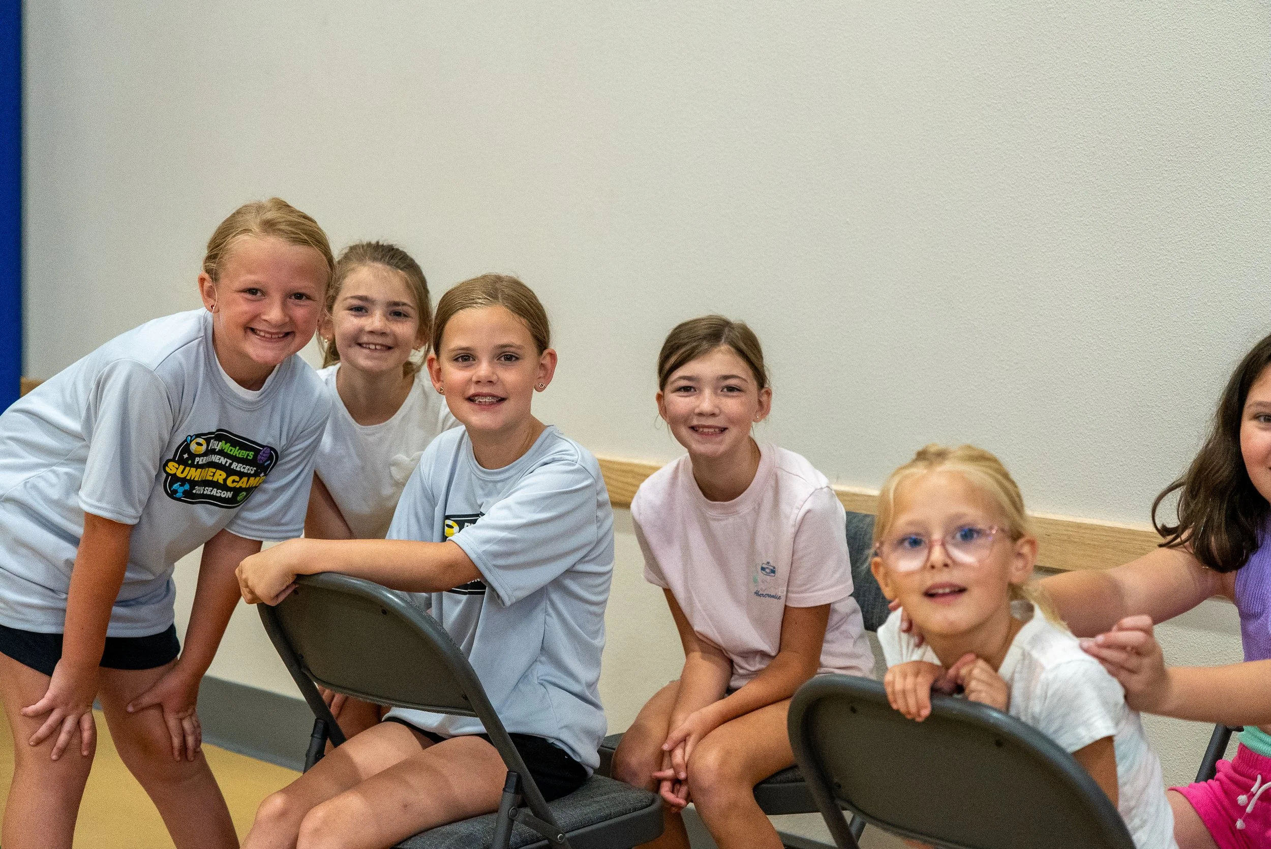 A group of smiling children sitting and standing around a table in a classroom or community room.