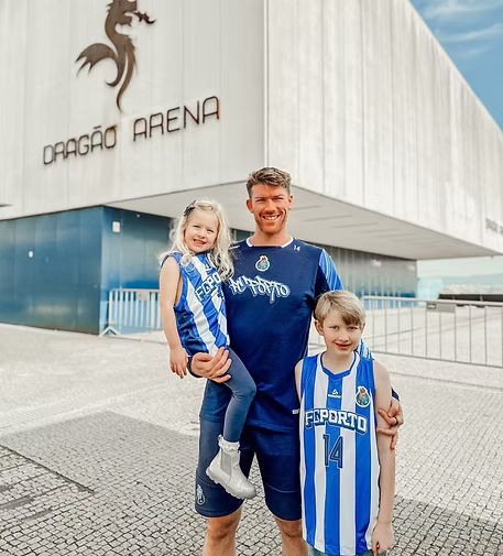 A man and two children standing in front of Dragão Arena, all wearing blue sports jerseys.