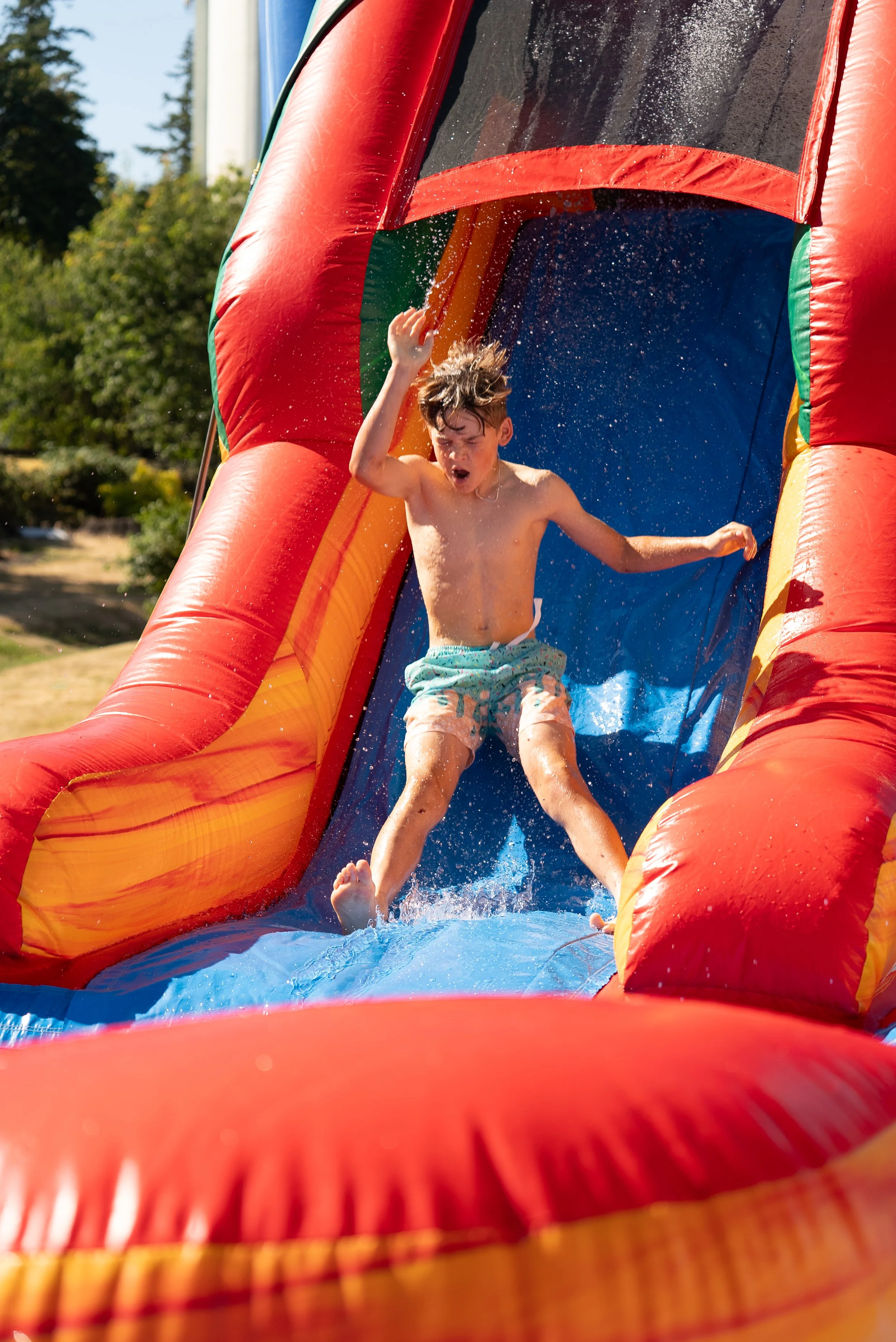 Child sliding down an inflatable water slide outdoors on a sunny day.