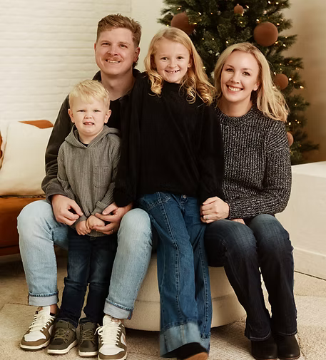 Family of four sitting together in front of a decorated Christmas tree.