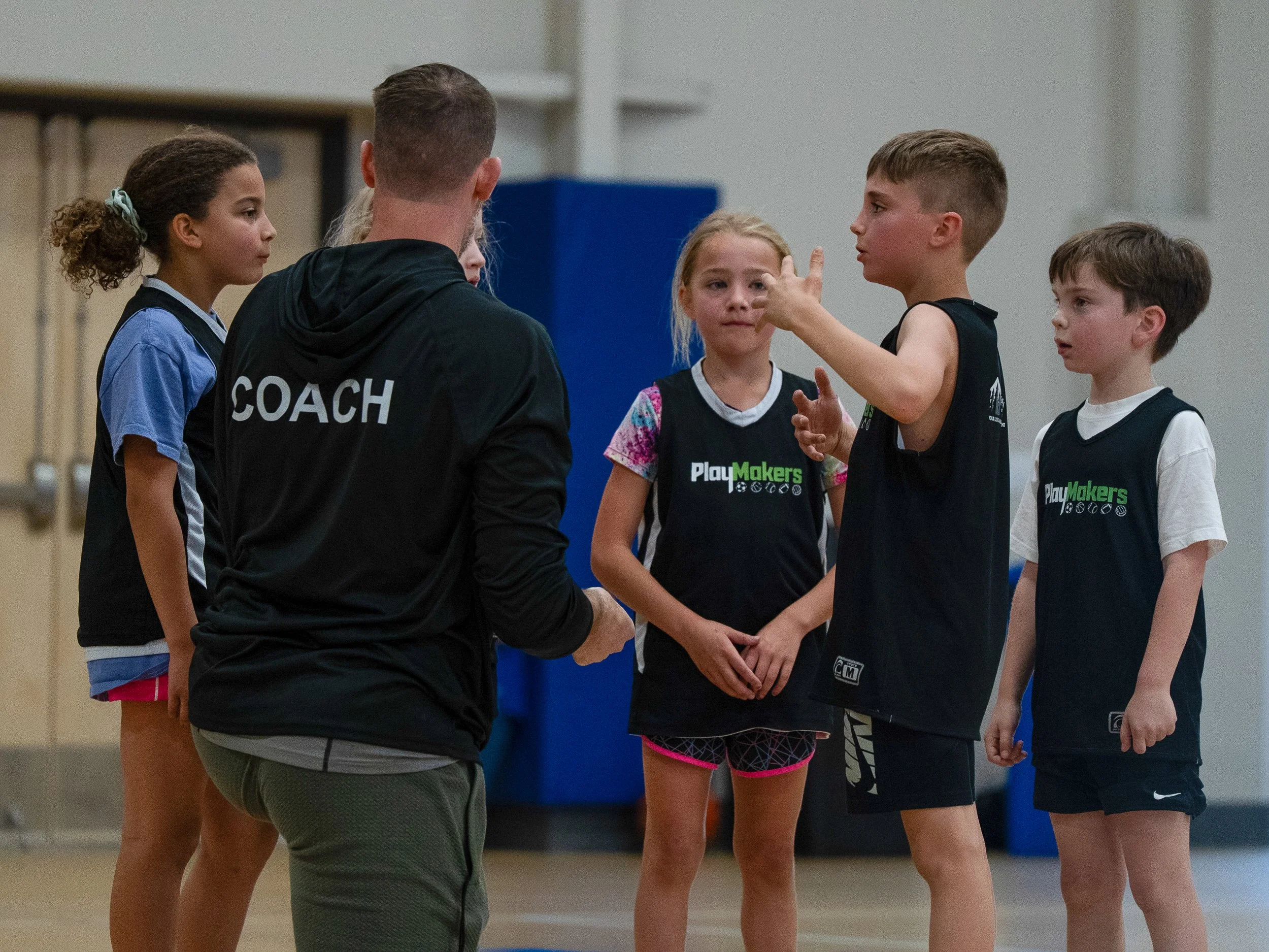 A coach speaking to a group of young athletes in a gymnasium.