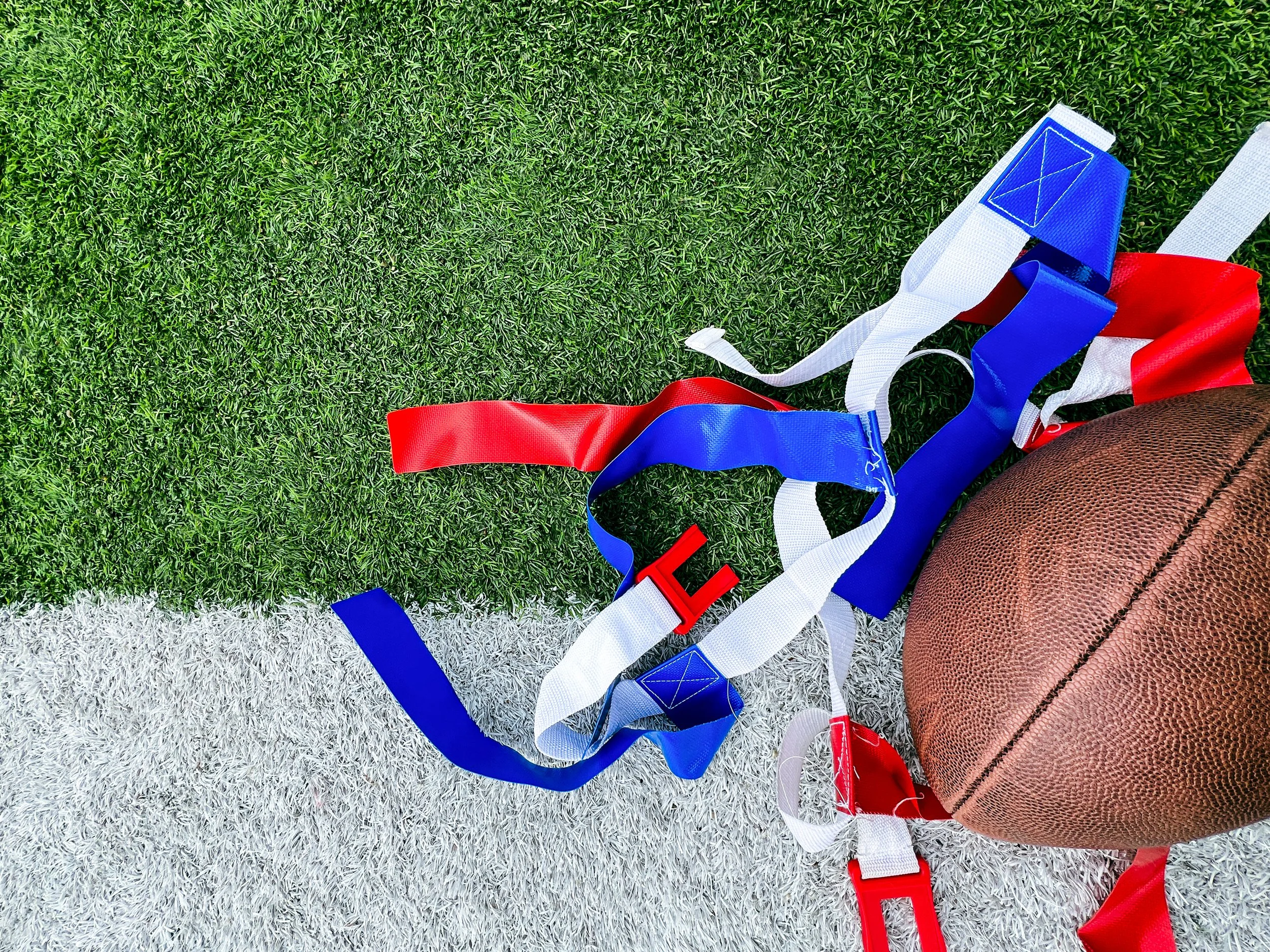 American football lying on artificial turf with various colored straps or laces nearby.