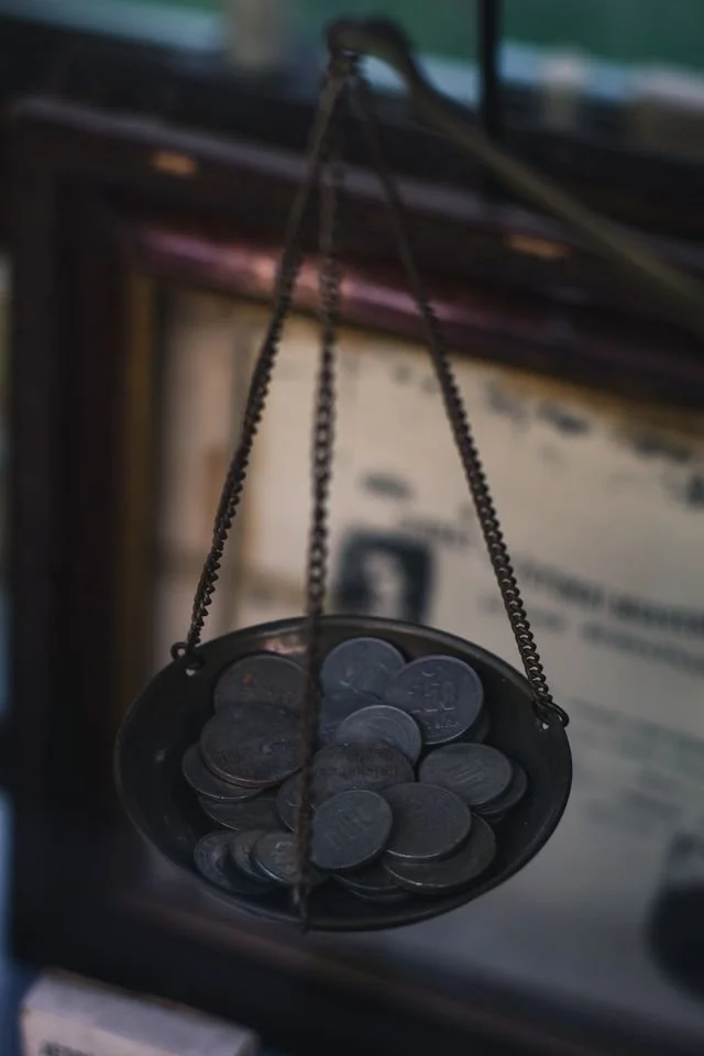 A small balance scale holding several coins, hanging from a chain.