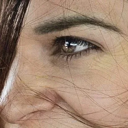 A close-up of a woman's eye and part of her face, with her hair partially covering her face.