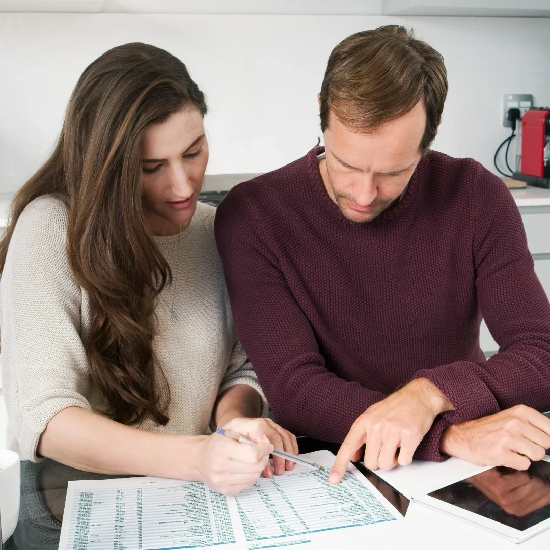 A woman and a man looking at financial documents, the woman is holding a pen and pointing to the papers while the man points at something on the documents.