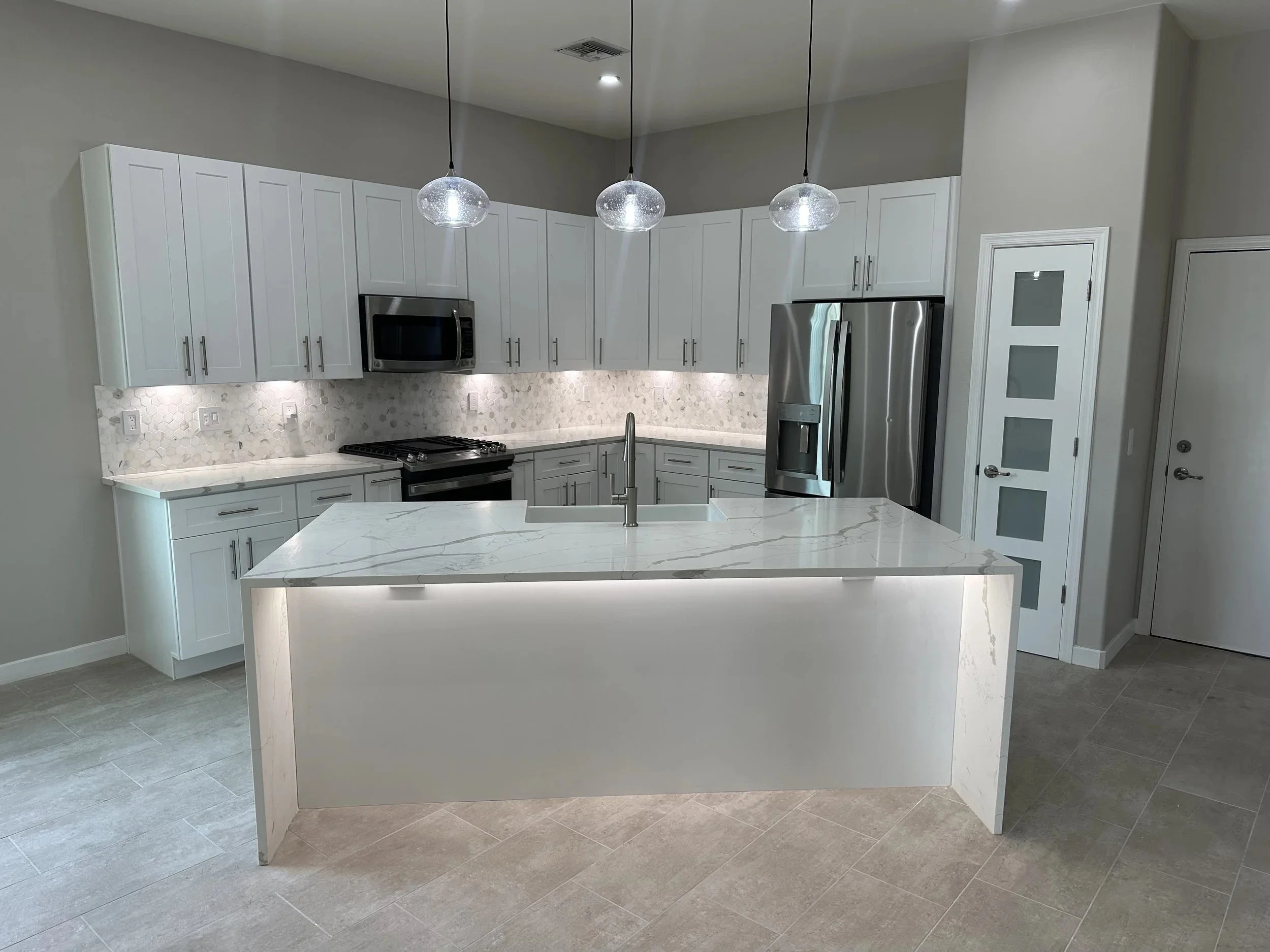 Modern kitchen with white cabinets, marble island, stainless steel appliances, and pendant lighting