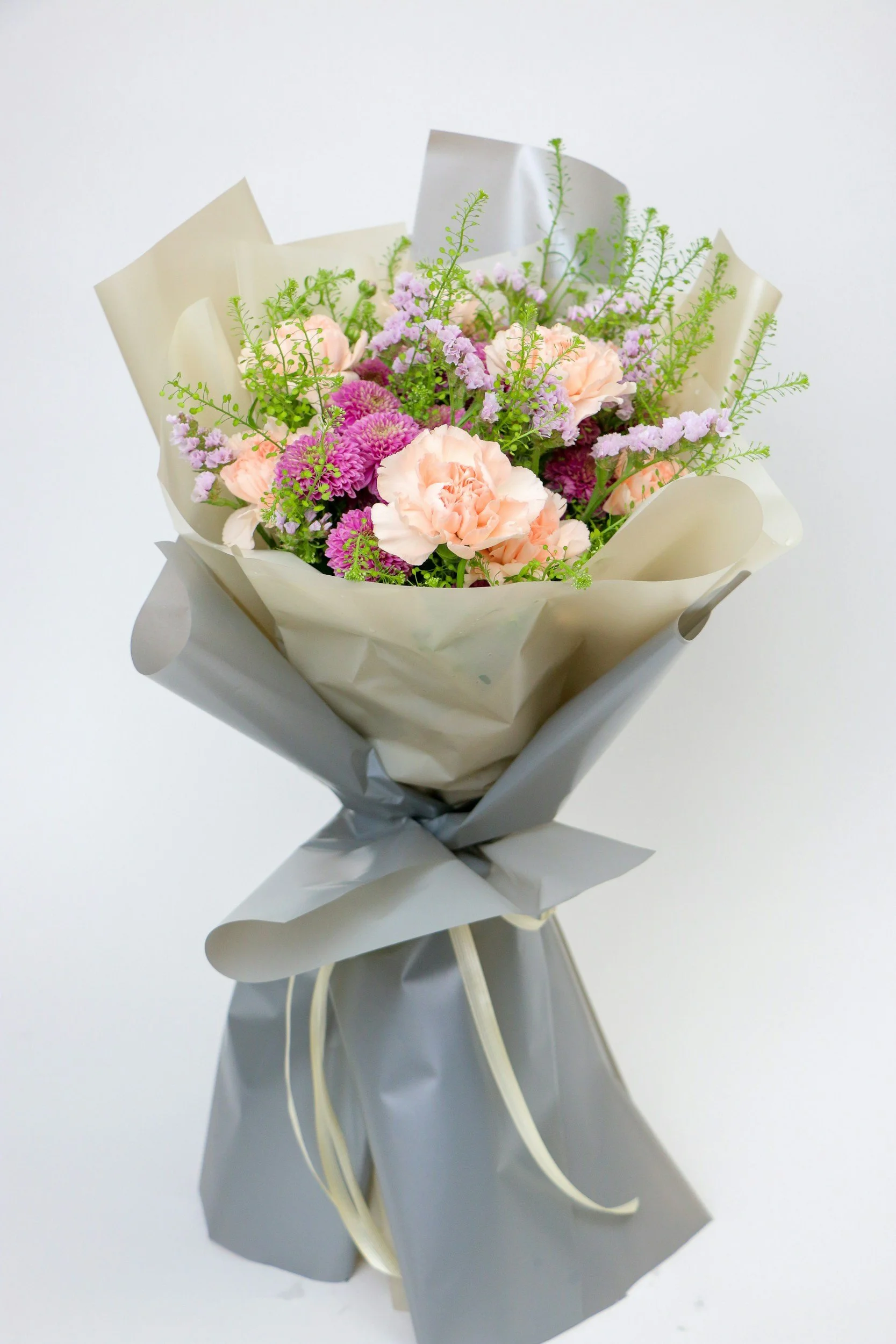 A bouquet of pink, purple, and peach flowers wrapped in gray and white paper.