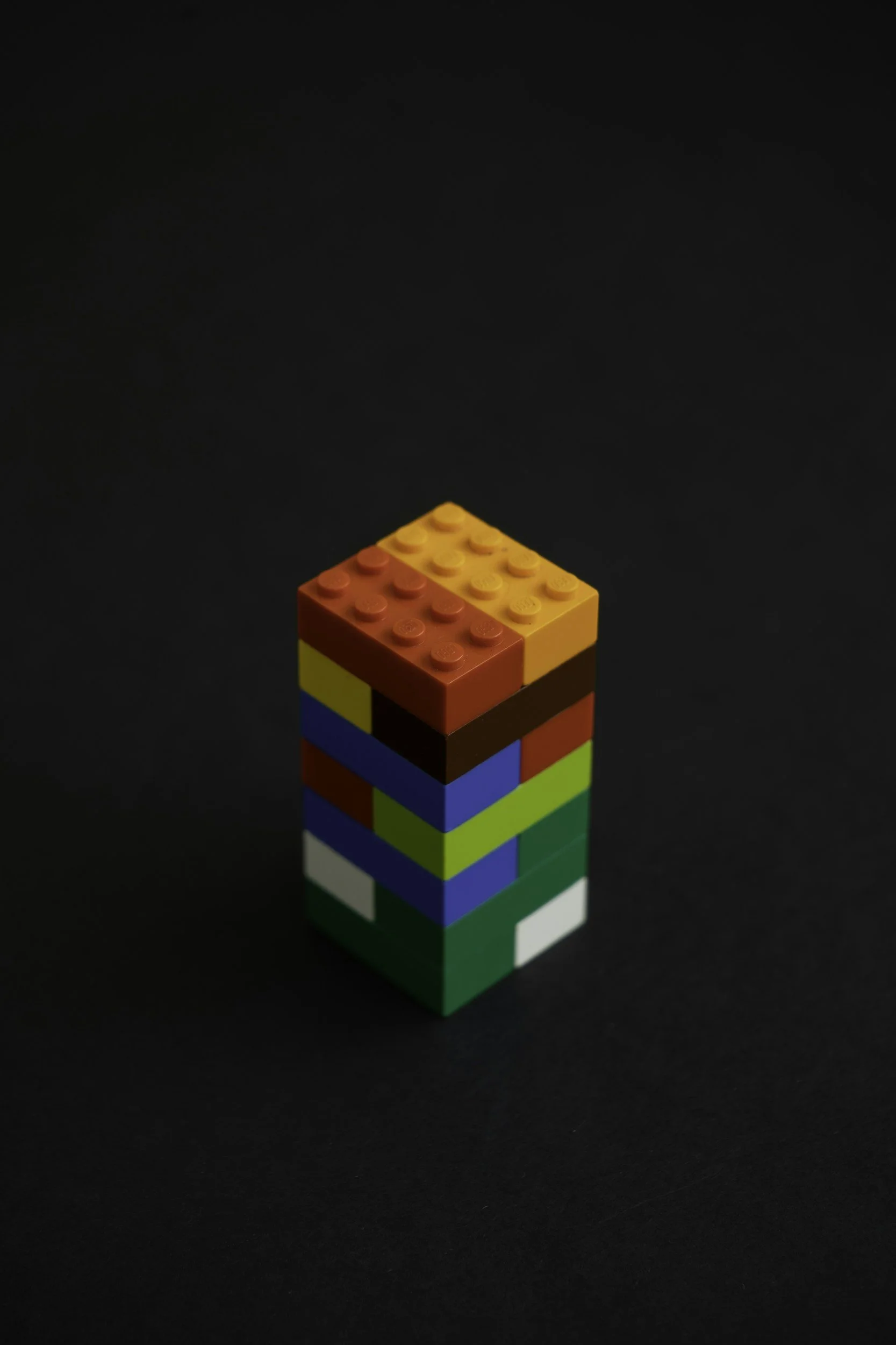 Colorful plastic toy block tower on a black background with a gradient lighting effect.