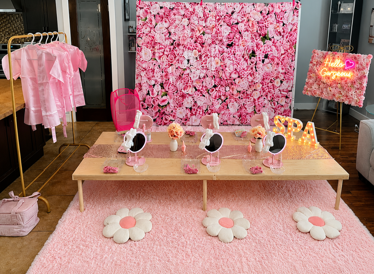 Decorated room with pink and white floral theme, pink shirts on a clothing rack, pink vanity mirrors, flower-shaped cushions on a pink carpet, and neon signs reading "Hello Gorgeous" and "SPA."