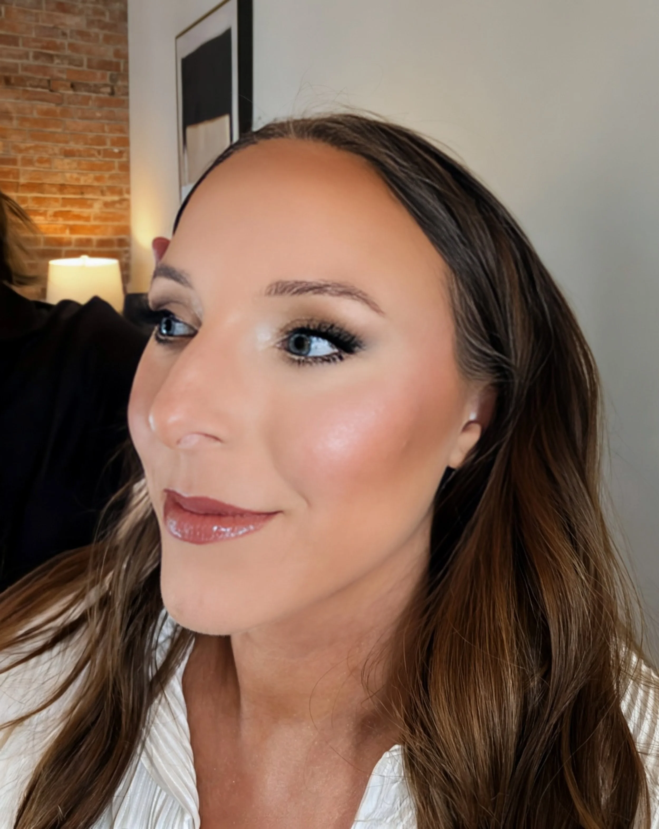 Close-up of a woman with brown hair, blue eyes, wearing eye makeup and lipstick, smiling slightly.