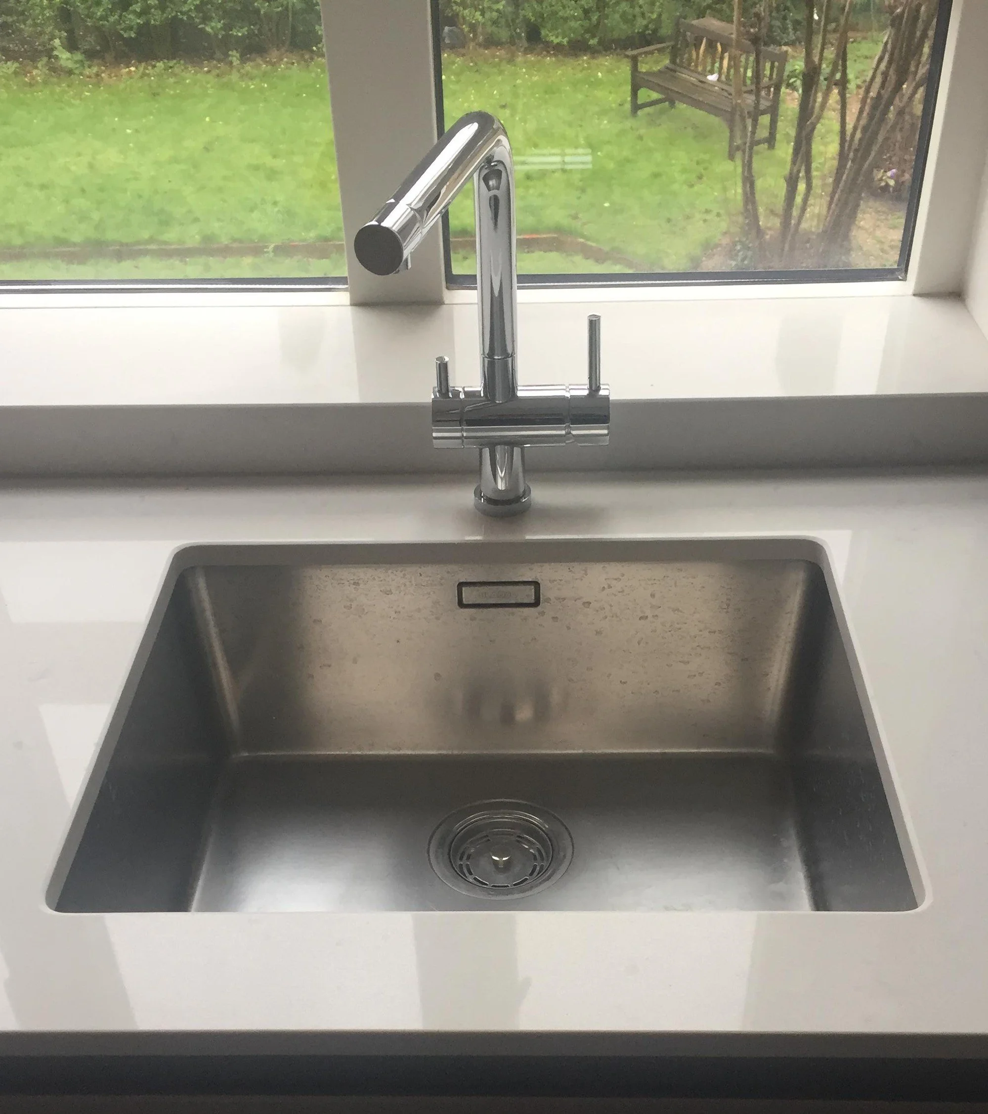 Kitchen sink with a chrome faucet and a view of a rainy backyard through a window.