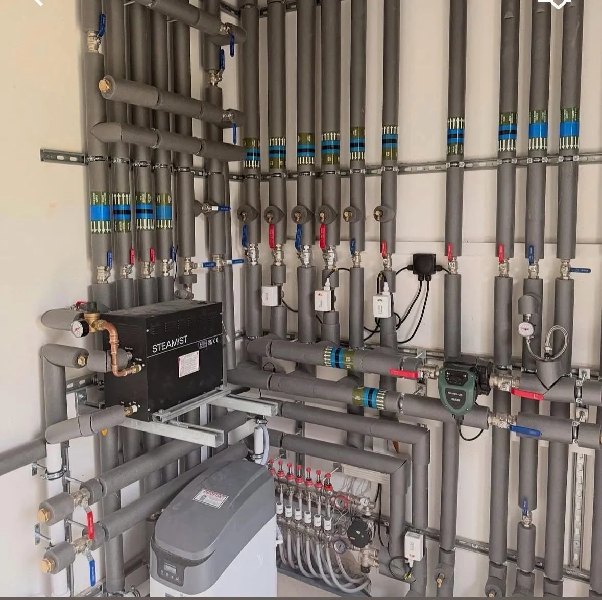 Complex plumbing system with numerous pipes, valves, gauges, and control units.