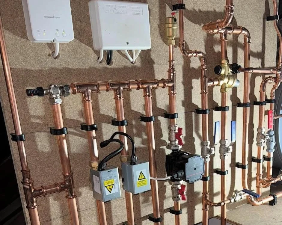 A complex setup of copper piping with various valves, meters, and electrical components for plumbing or heating system installation.