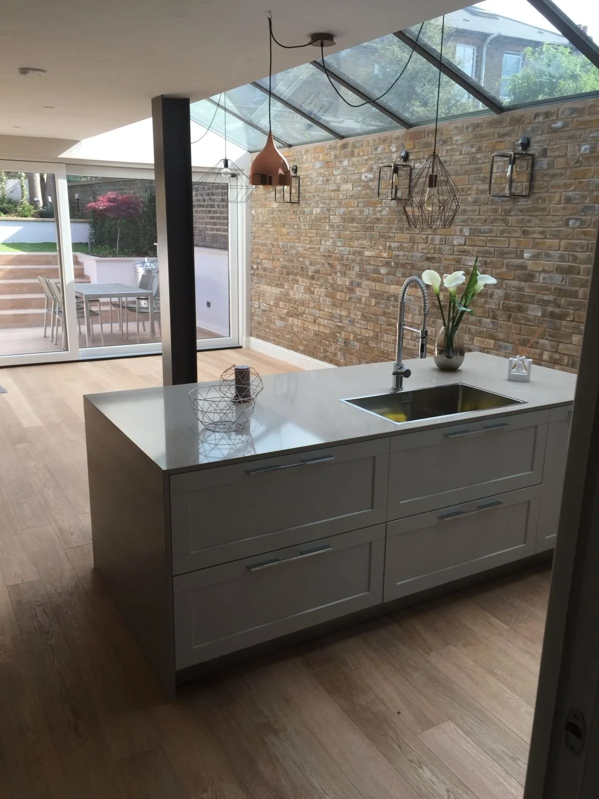 Modern kitchen with white island, brick wall, and skylight ceiling, view of outdoor patio with table and chairs.