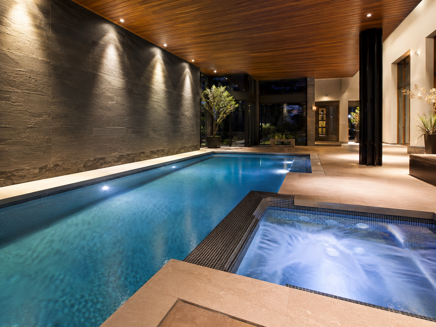 Indoor pool area with a hot tub, modern minimalist decor, wooden ceiling, and ambient lighting.