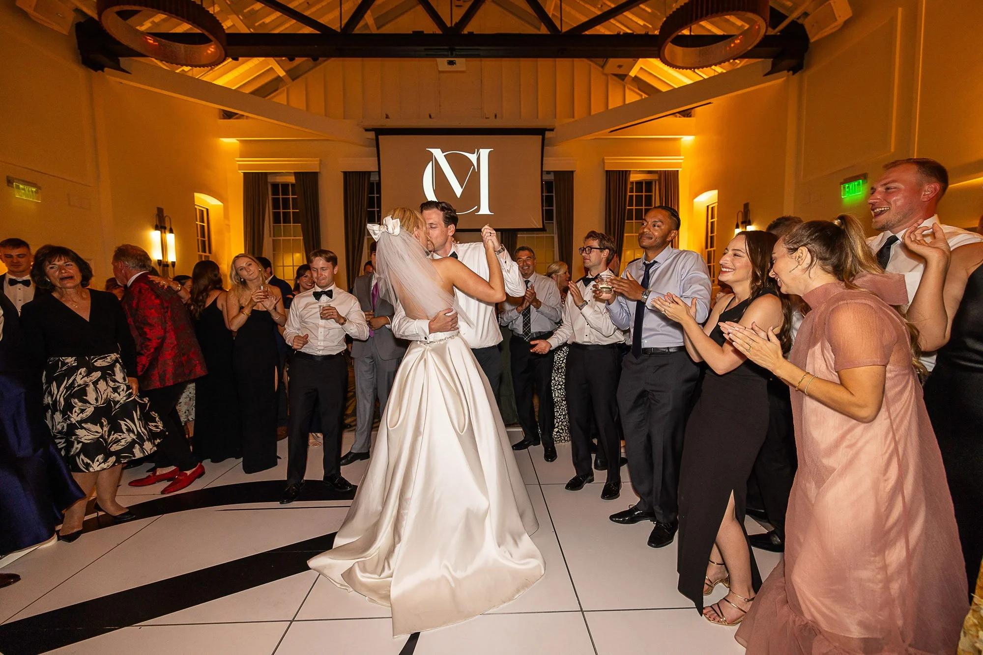 A bride and groom kiss on the dance floor as guests gather around them, smiling and clapping at a wedding reception at Cavallo Point in Sausalito, CA.