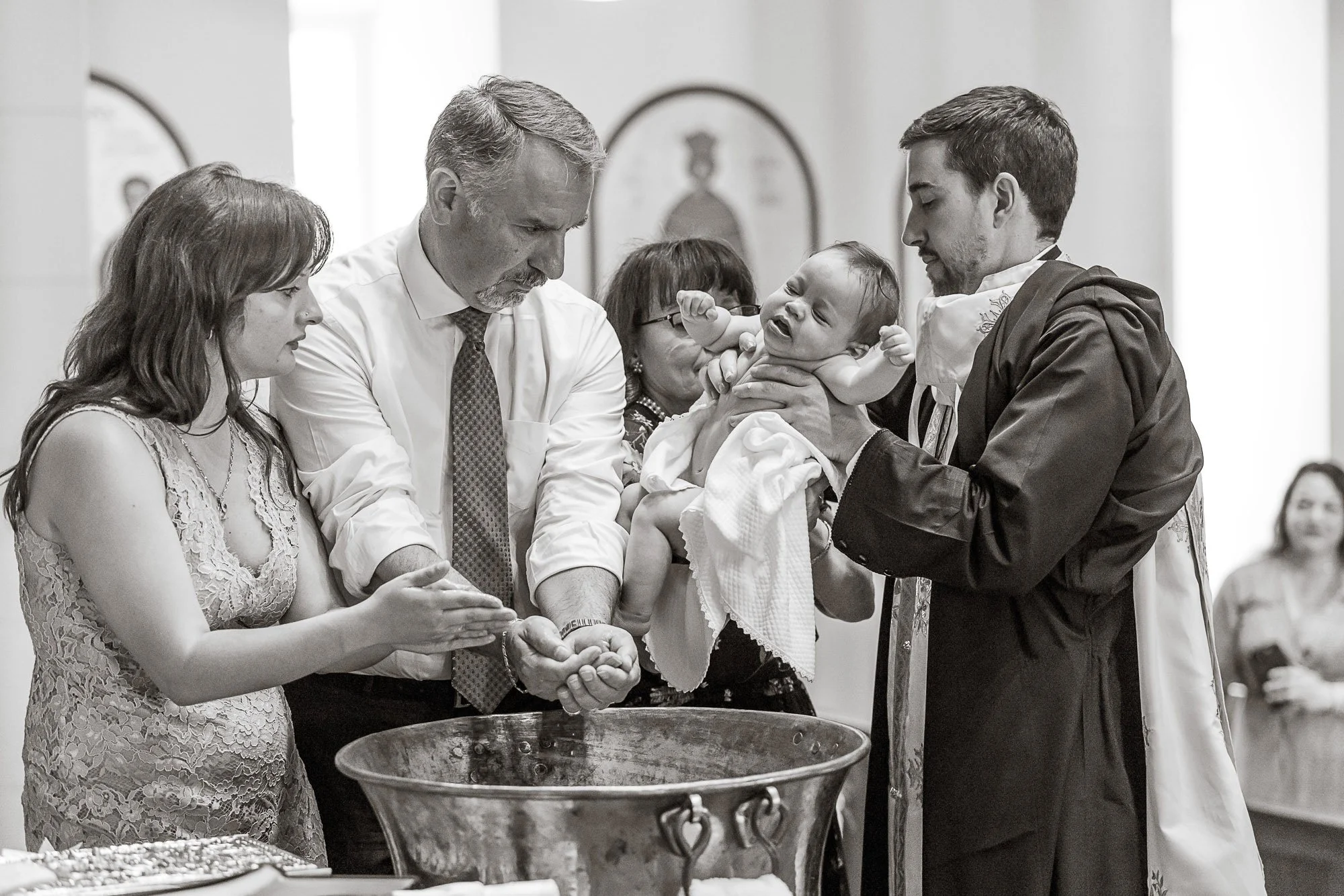 A baptism ceremony involving a baby held by a woman, with two men and another woman gathered around in a church setting.