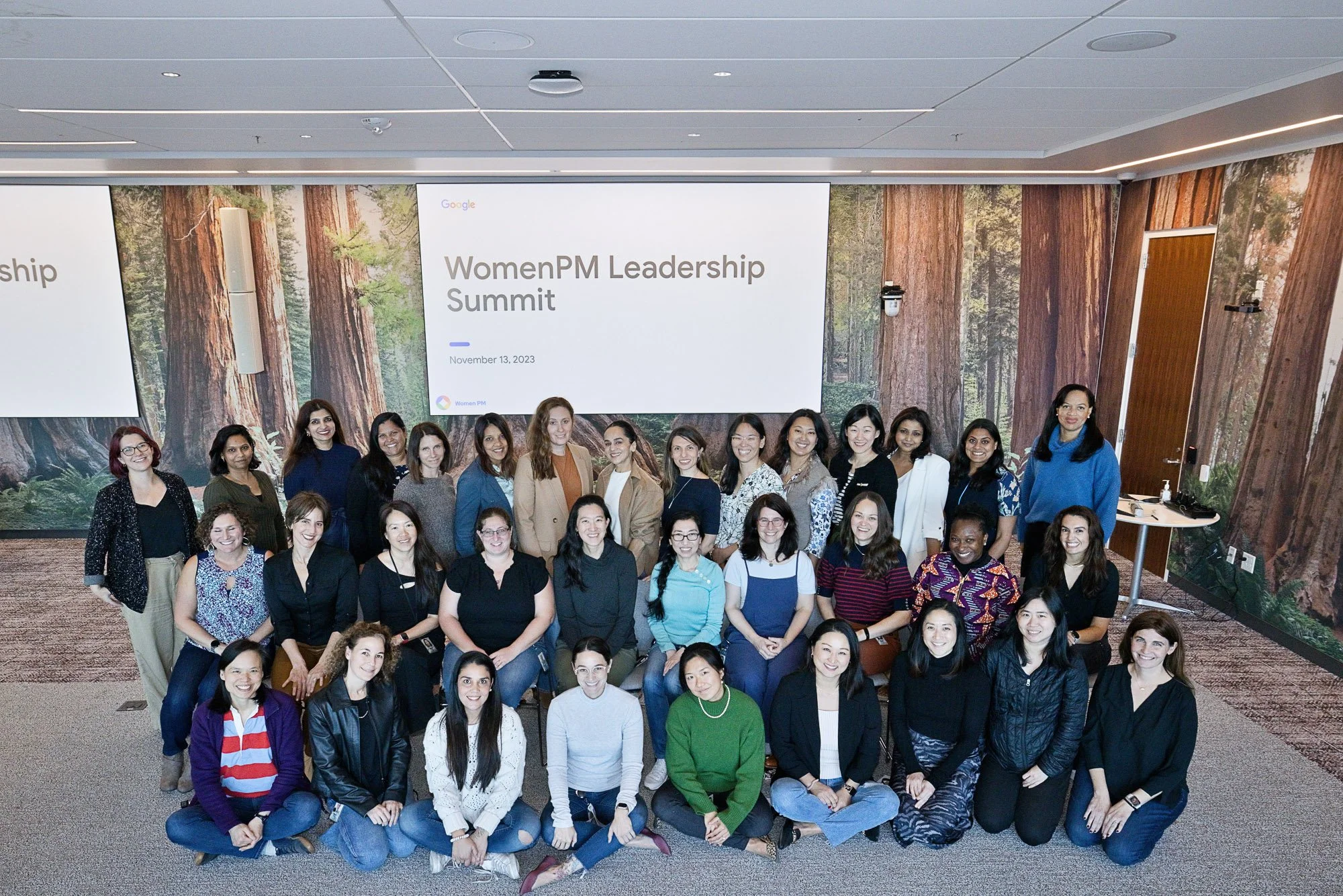 A group of women posing for a photo in front of a large forest-themed backdrop at the Women PM Leadership Summit on November 13, 2023.