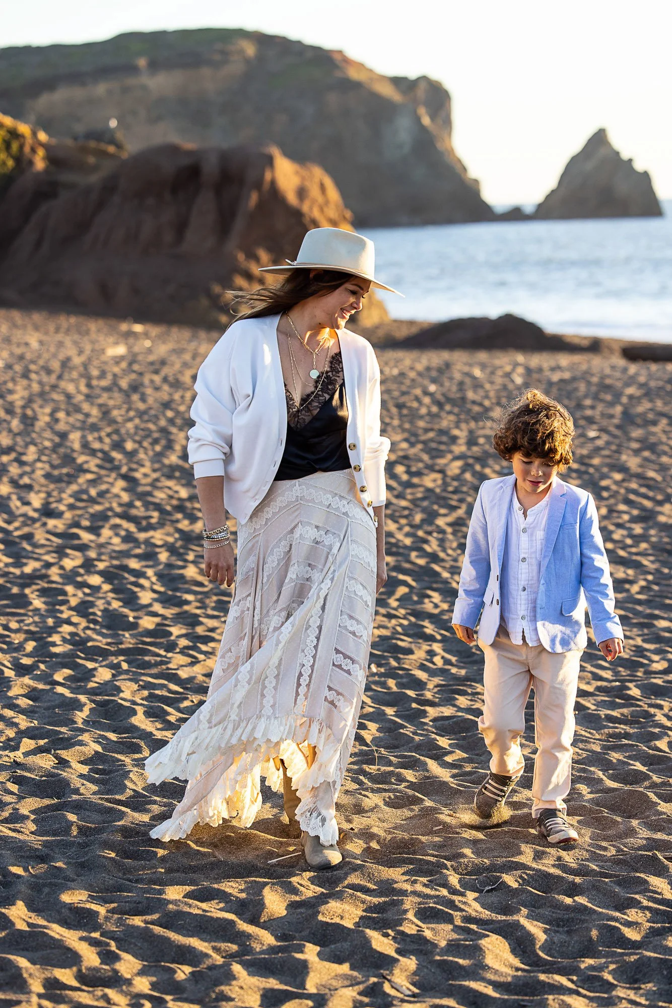A woman and a young boy walking on a sandy beach during sunset with rocky cliffs in the background at Rodeo Beach in Marin California.