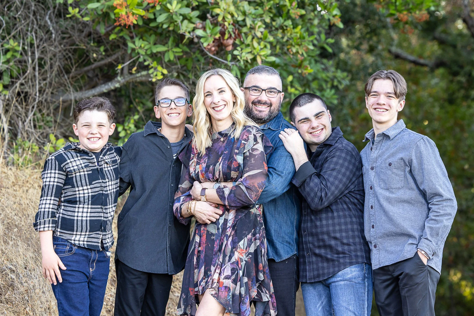 A group of six people, four men and two women, standing outdoors in front of green foliage, smiling and posing for the photo.