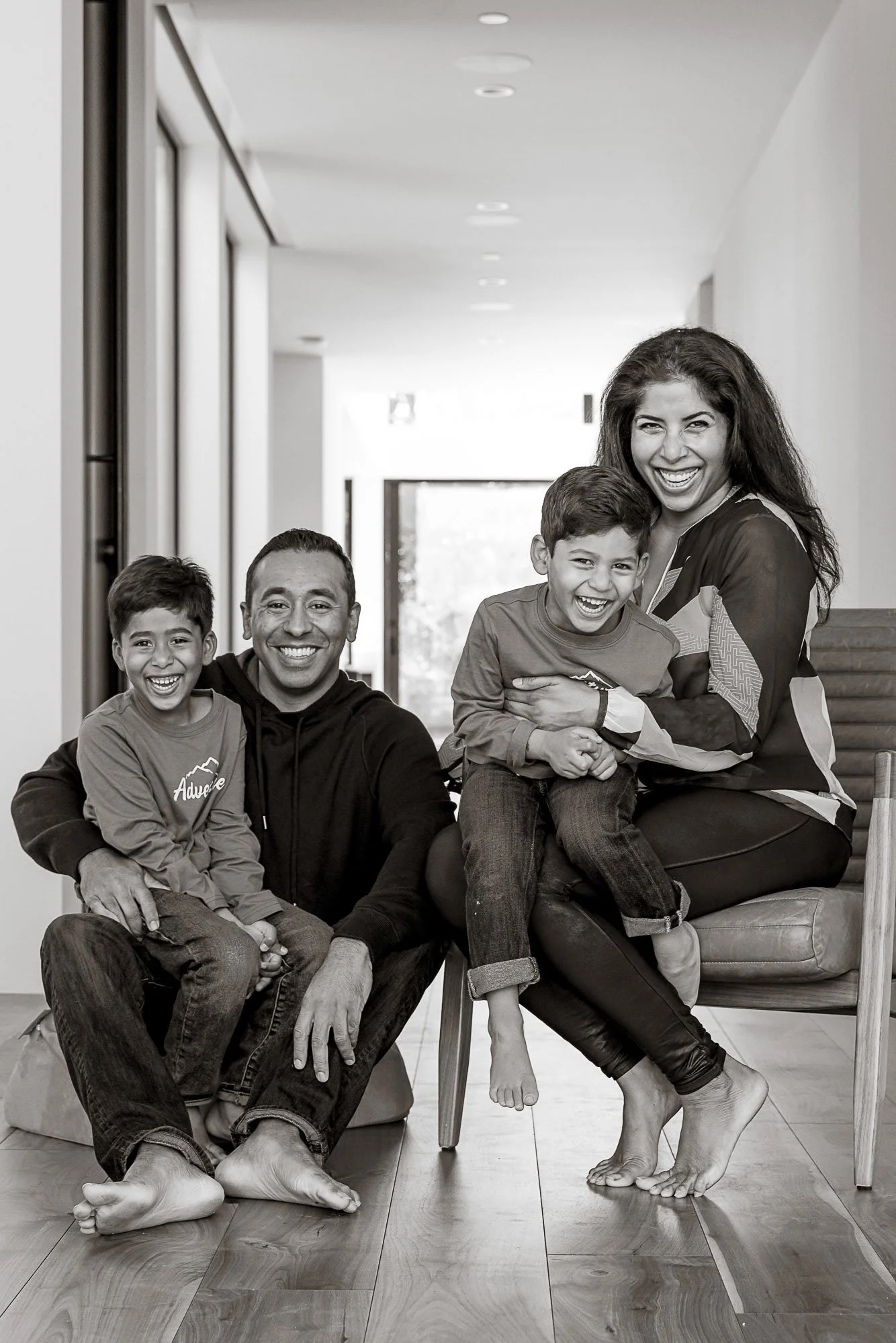 Family of four sitting together on the floor at home, laughing, black and white