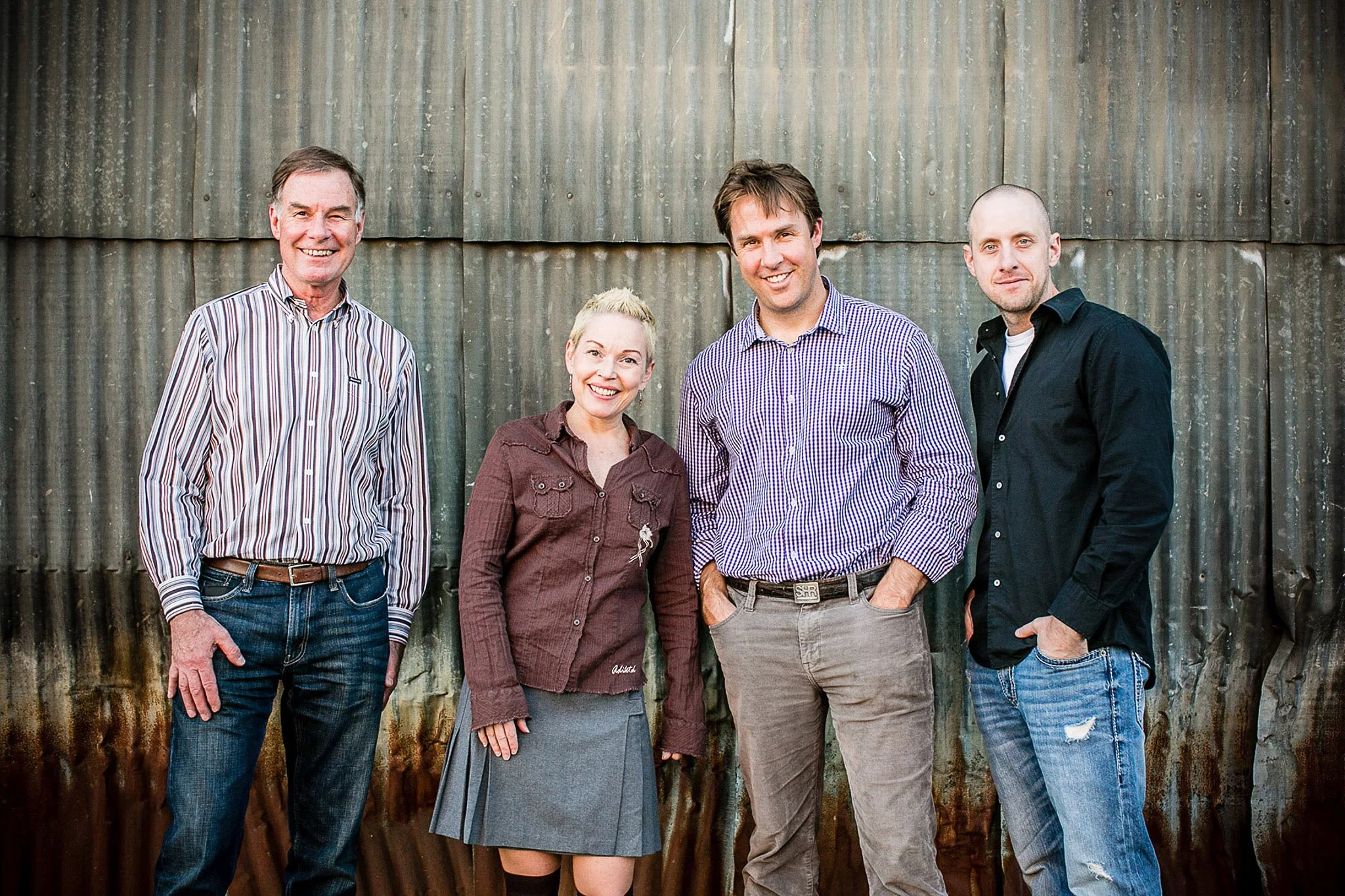 Five people standing in front of a corrugated metal wall, smiling and casually dressed.