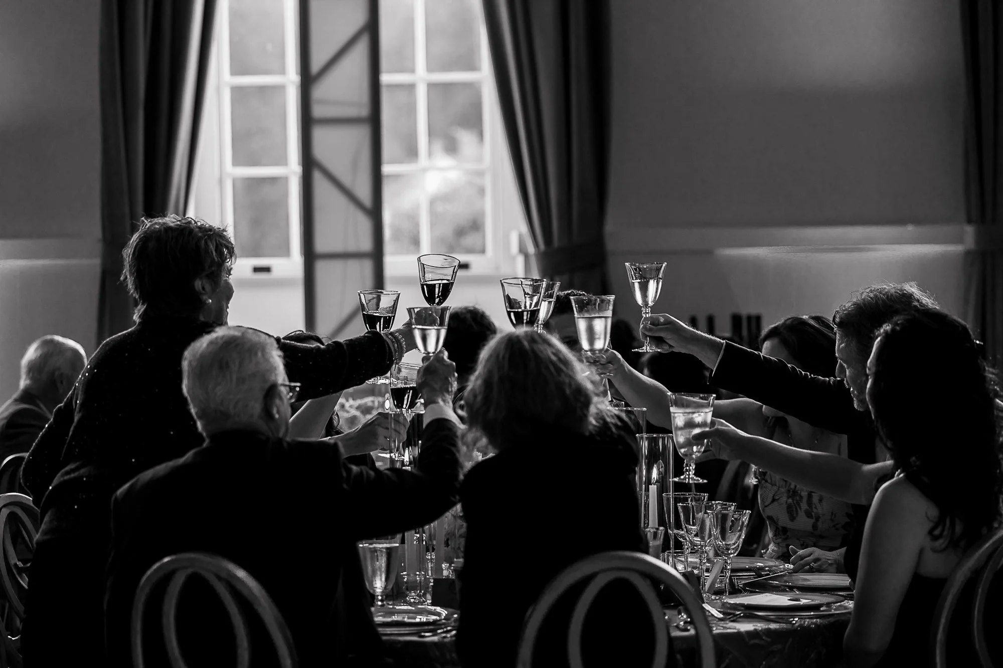 People gathered at a formal dinner raising their glasses in a toast, with a large window and dark curtains in the background at Cavallo Point in Sausalito, CA.