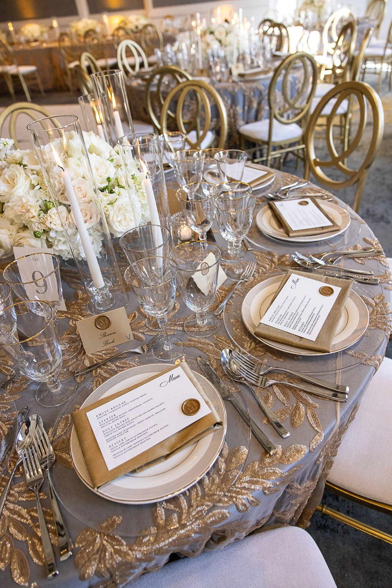 Elegant banquet table set for a wedding reception with white roses, candles, glassware, gold accents, and a menu card on each place setting at Cavallo Point in Sausalito, CA.