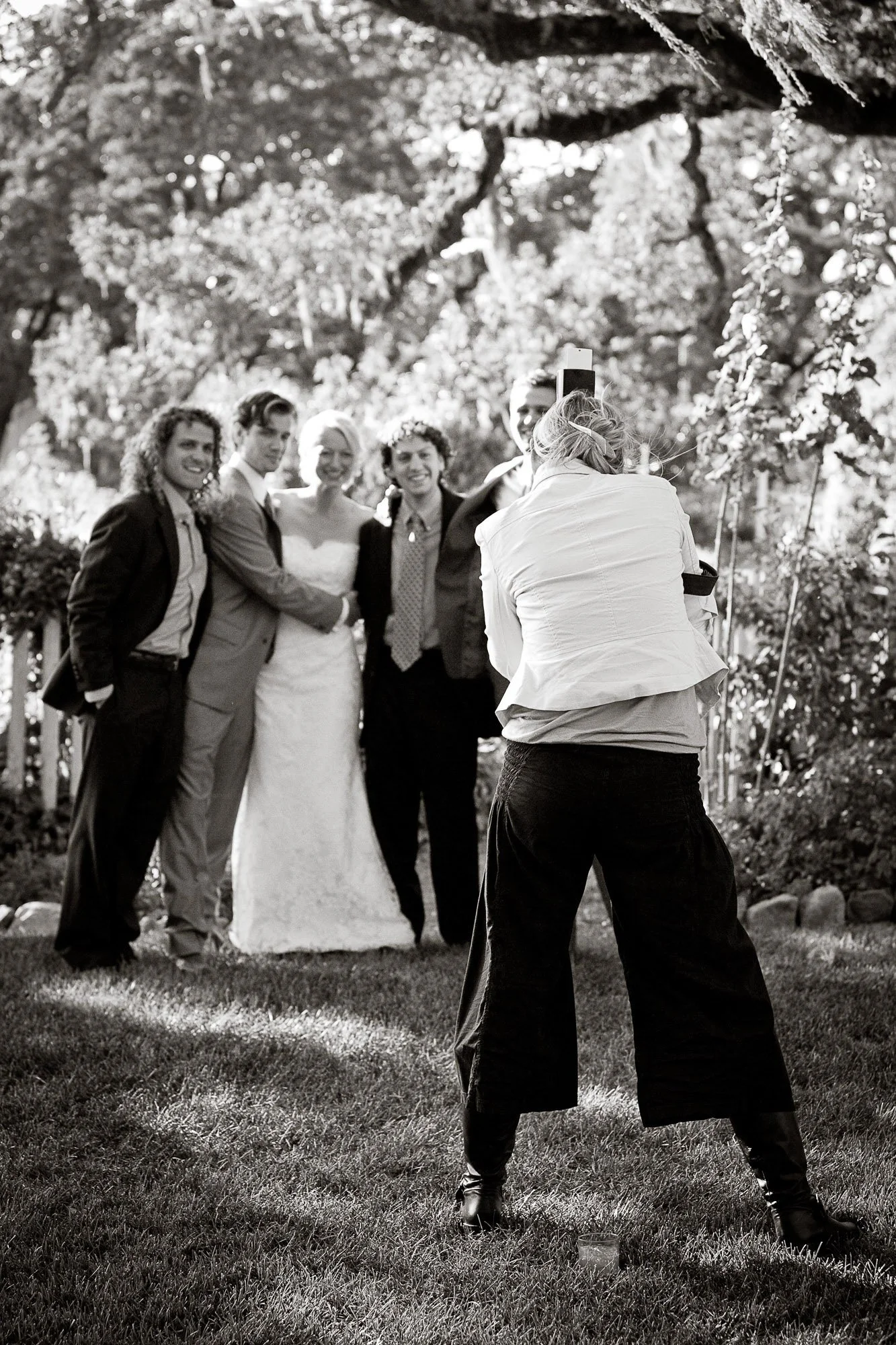 Tara Arrowood taking a picture of a wedding party outdoors with trees in the background.