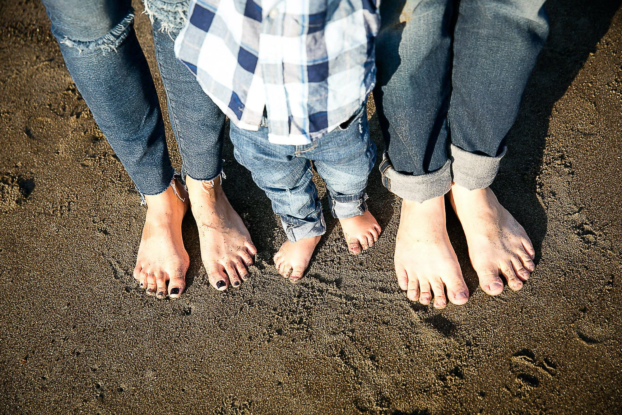 People standing barefoot on sand, with toes visible and some painted toenails, close-up shot.