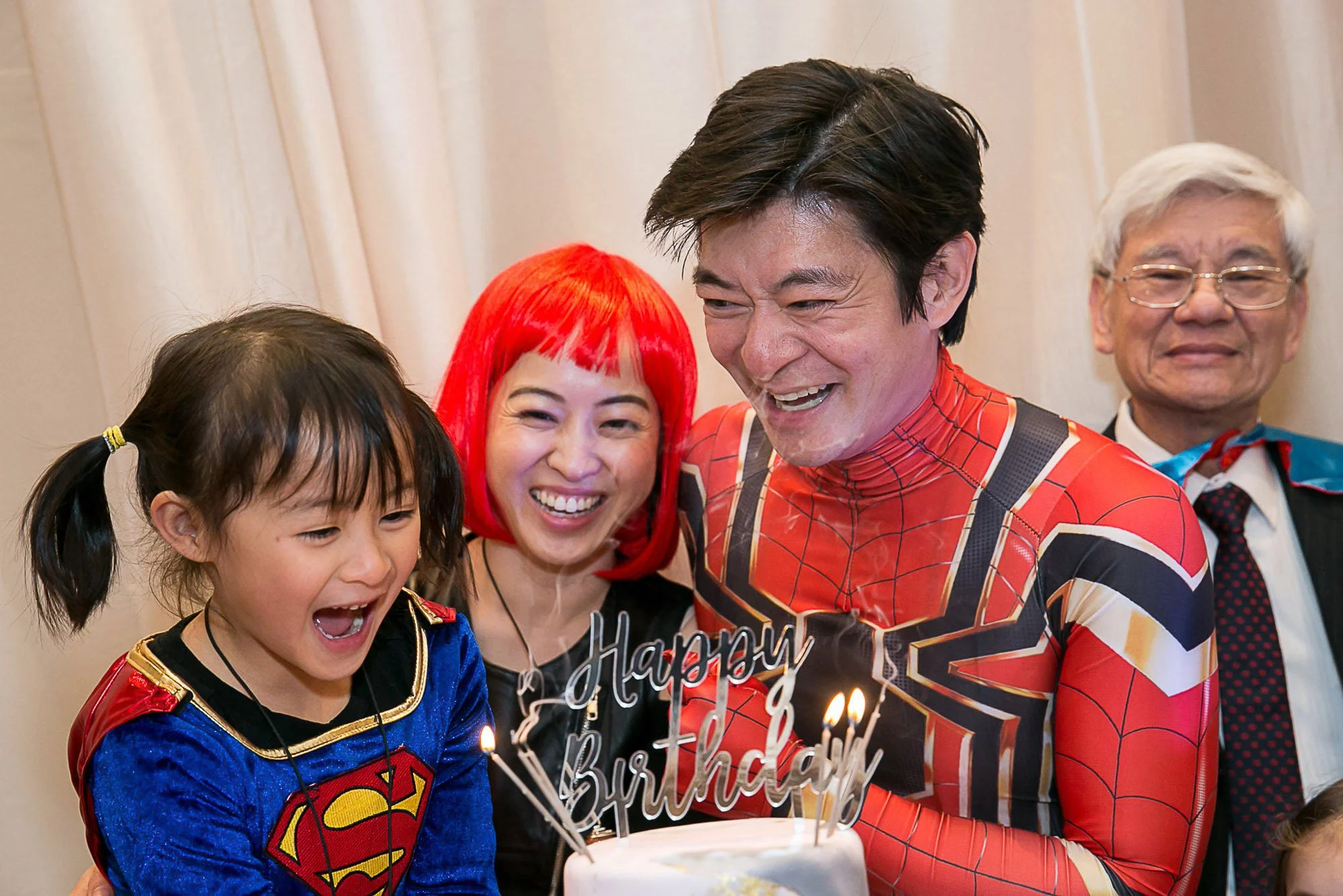 Kids in superhero costumes gathered around a birthday cake