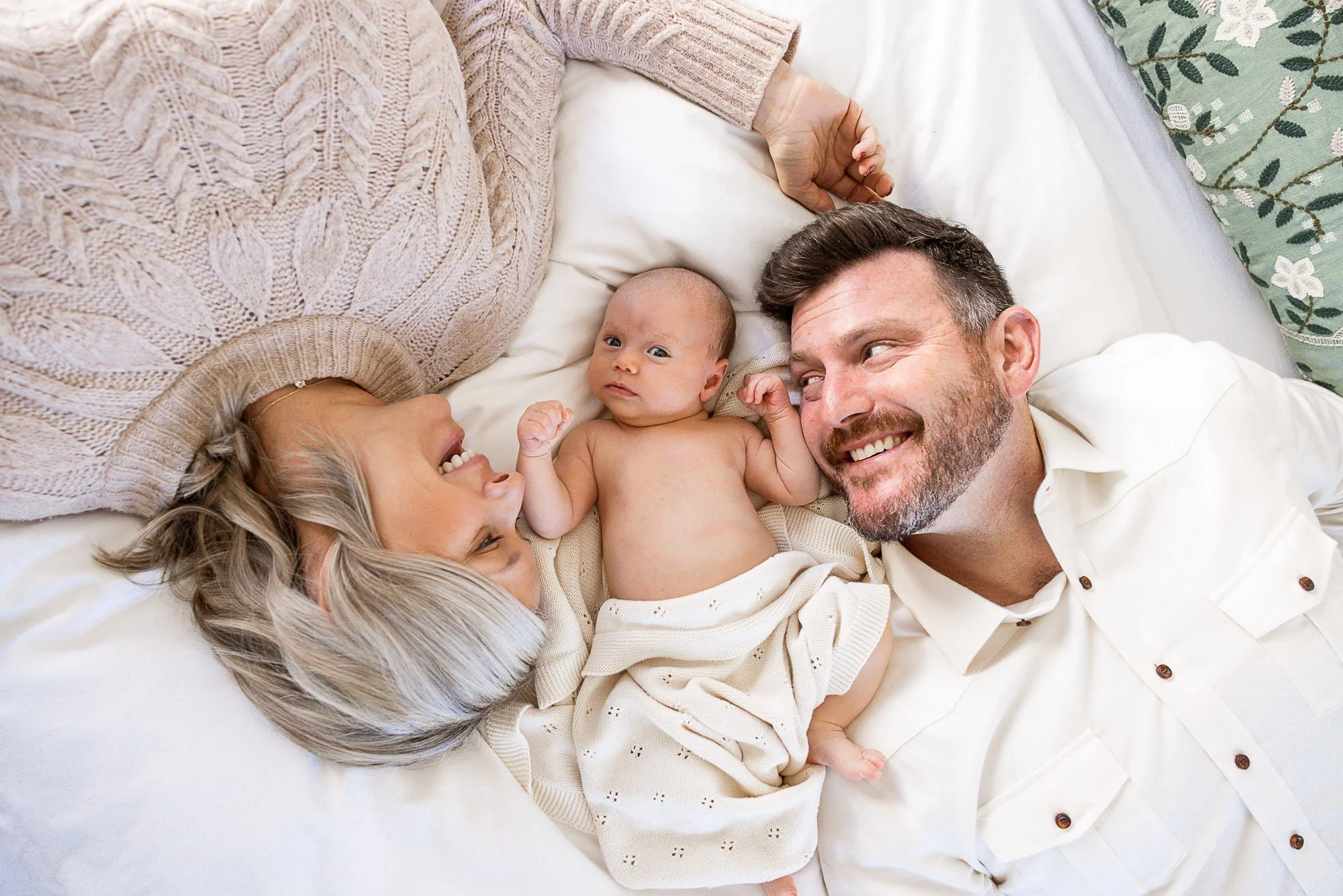 Parents lying beside their newborn on a bed at home