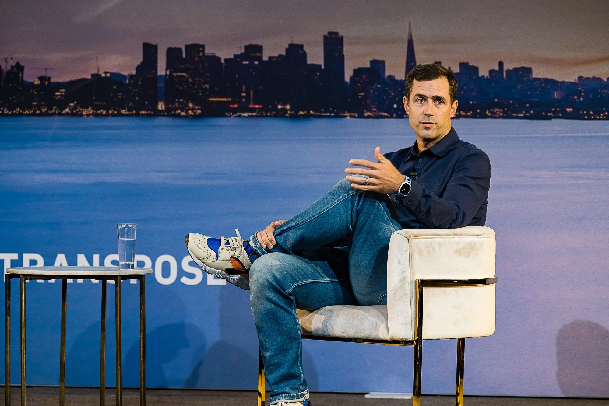 Speaker on stage during a fireside chat with the San Francisco skyline behind him