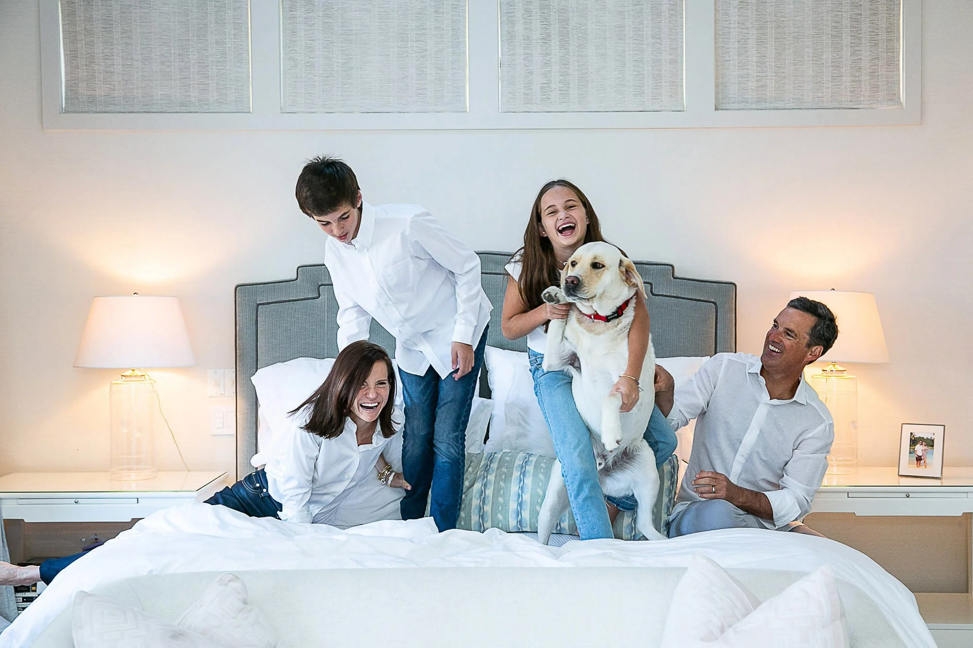 Family of four laughing on the bed at home with their yellow lab