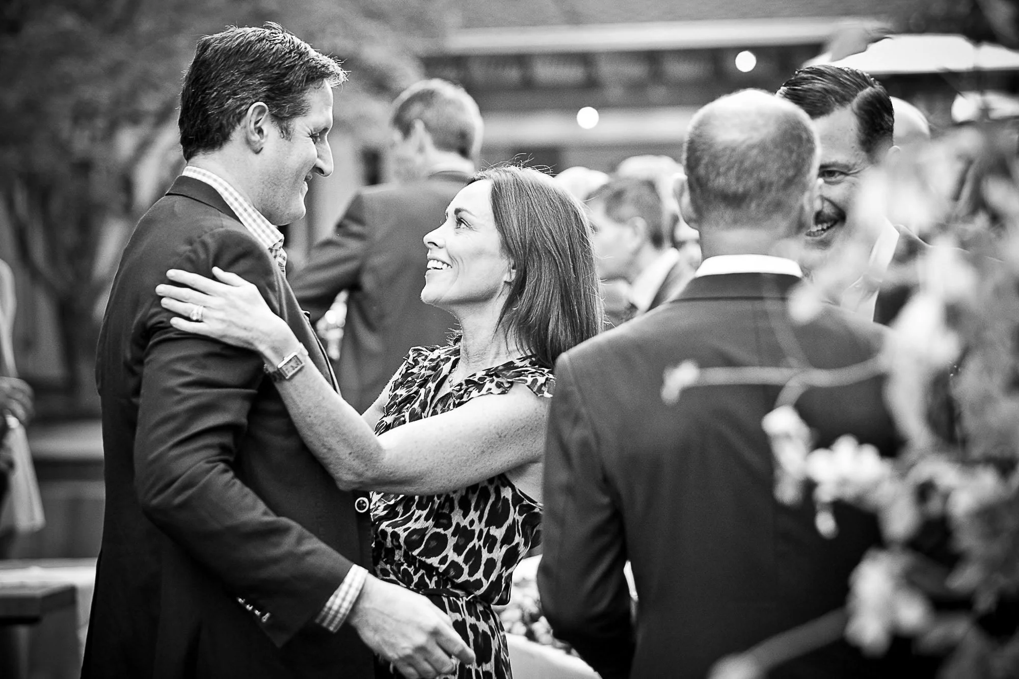 A smiling man and woman dancing together at a formal event, surrounded by other people also dancing and socializing.