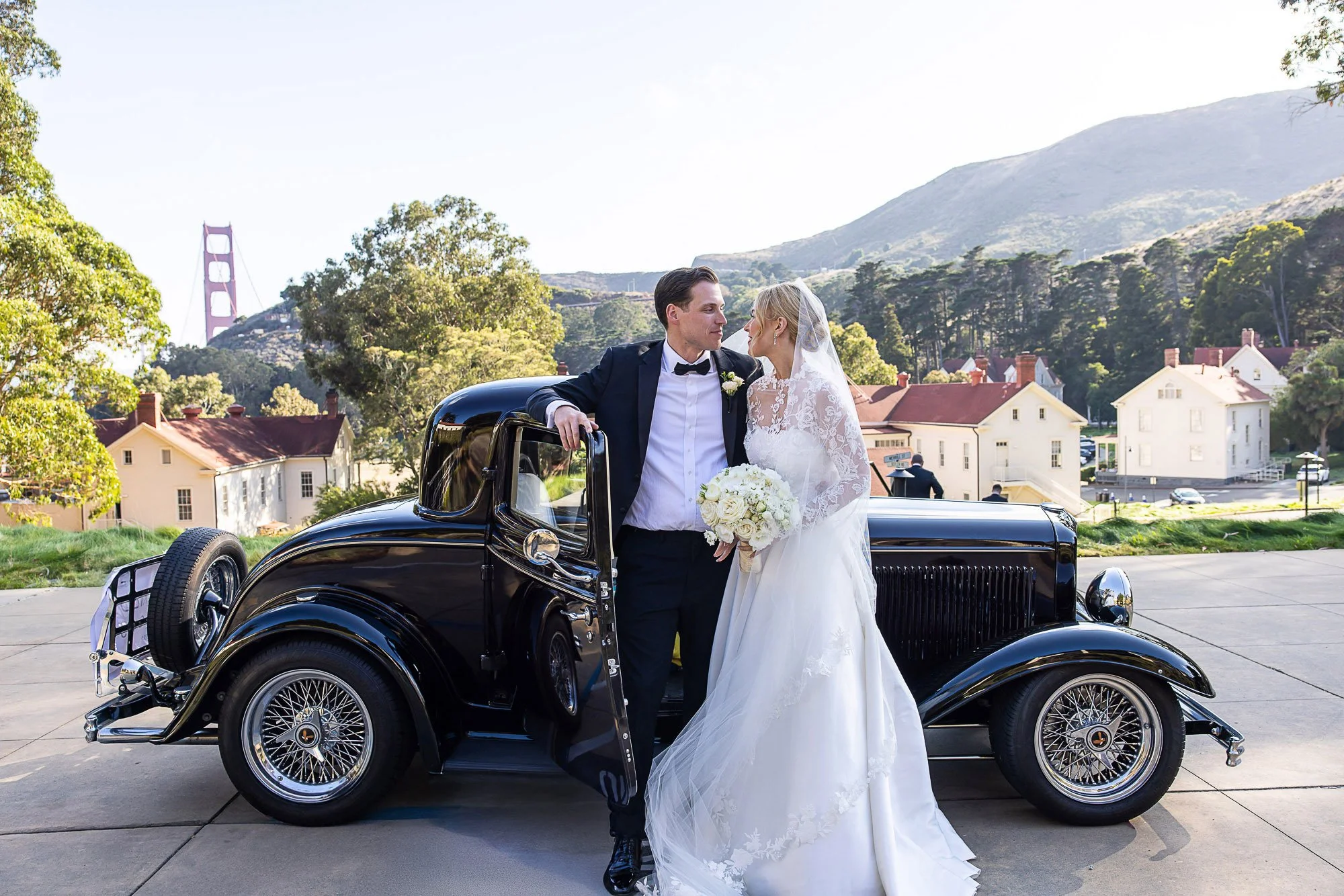 Bride and groom beside a vintage black car at Cavallo Point, Sausalito, with the Golden Gate Bridge behind them