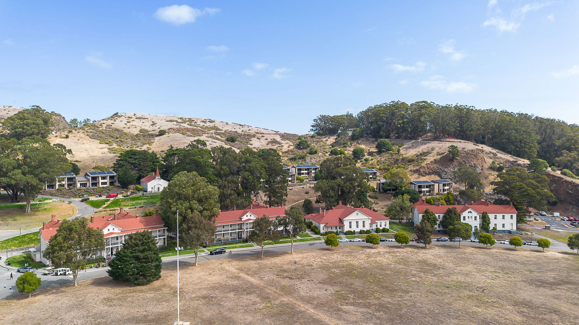 Residential area with red-roofed houses, trees, and a parking lot, set against a hillside with sparse vegetation and a clear blue sky at Cavallo Point in Sausalito, CA.