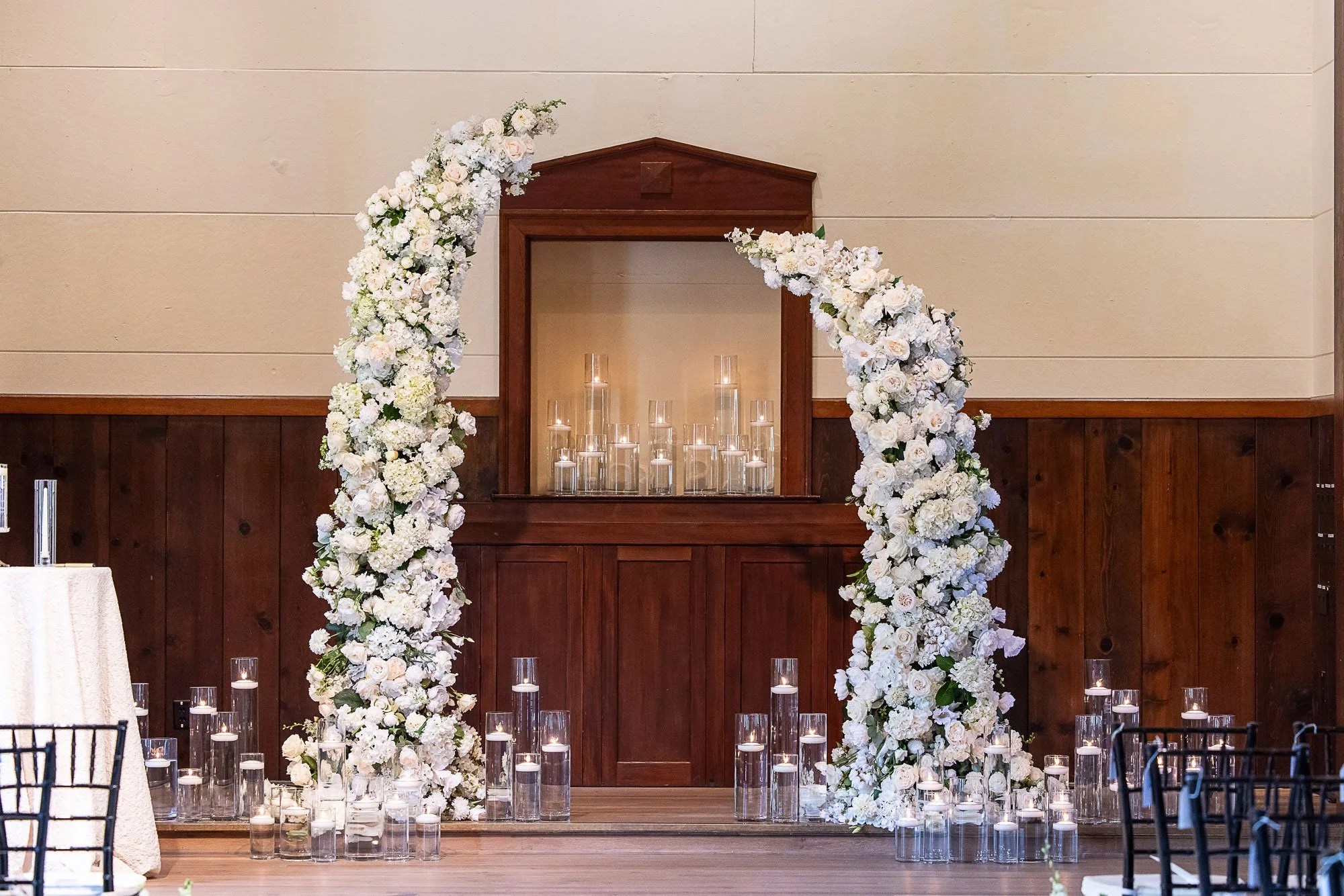 Indoor wedding ceremony setup with a floral arch of white flowers and candles at Cavallo Point in Sausalito, CA.