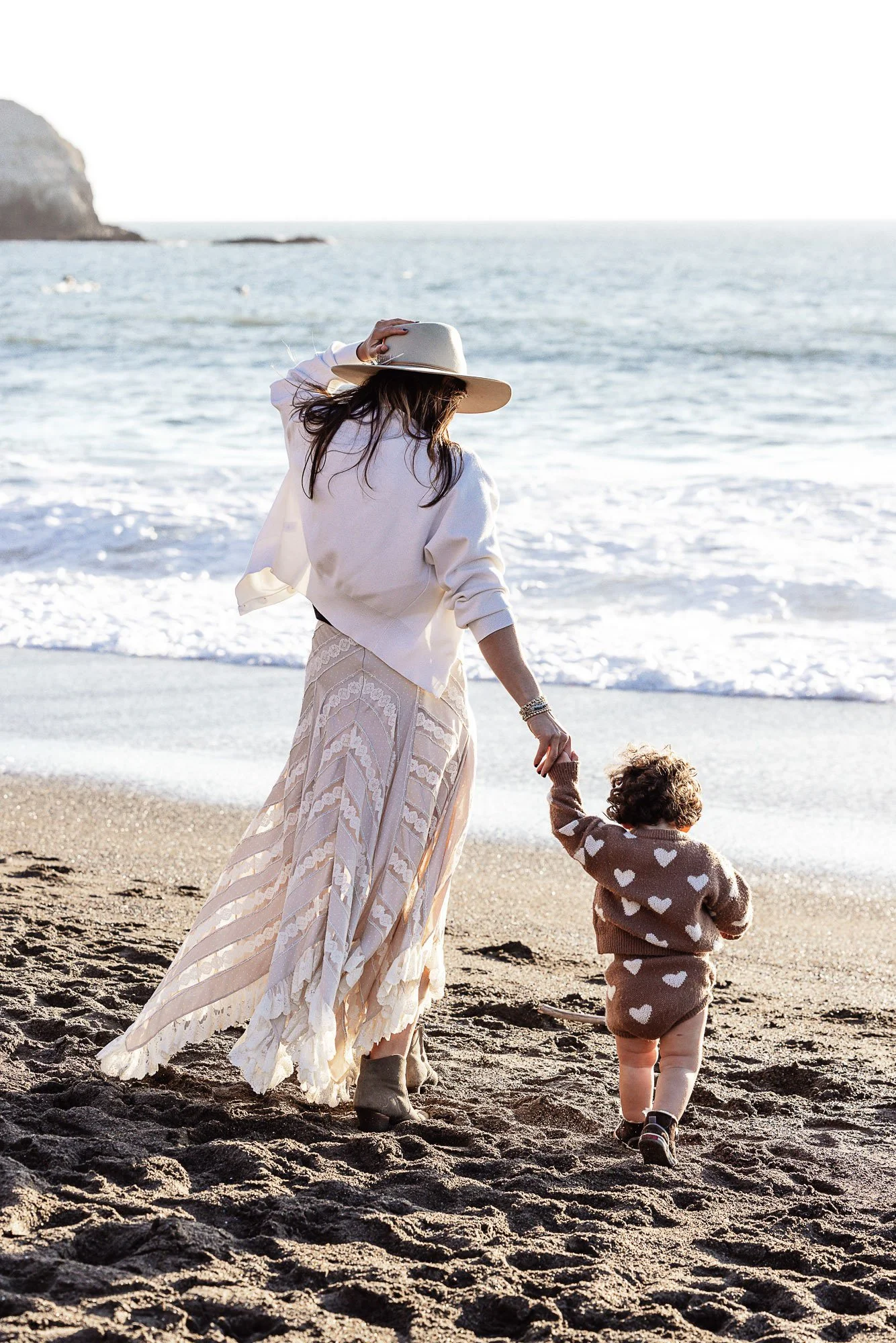 Mother and toddler walking hand in hand at the water's edge