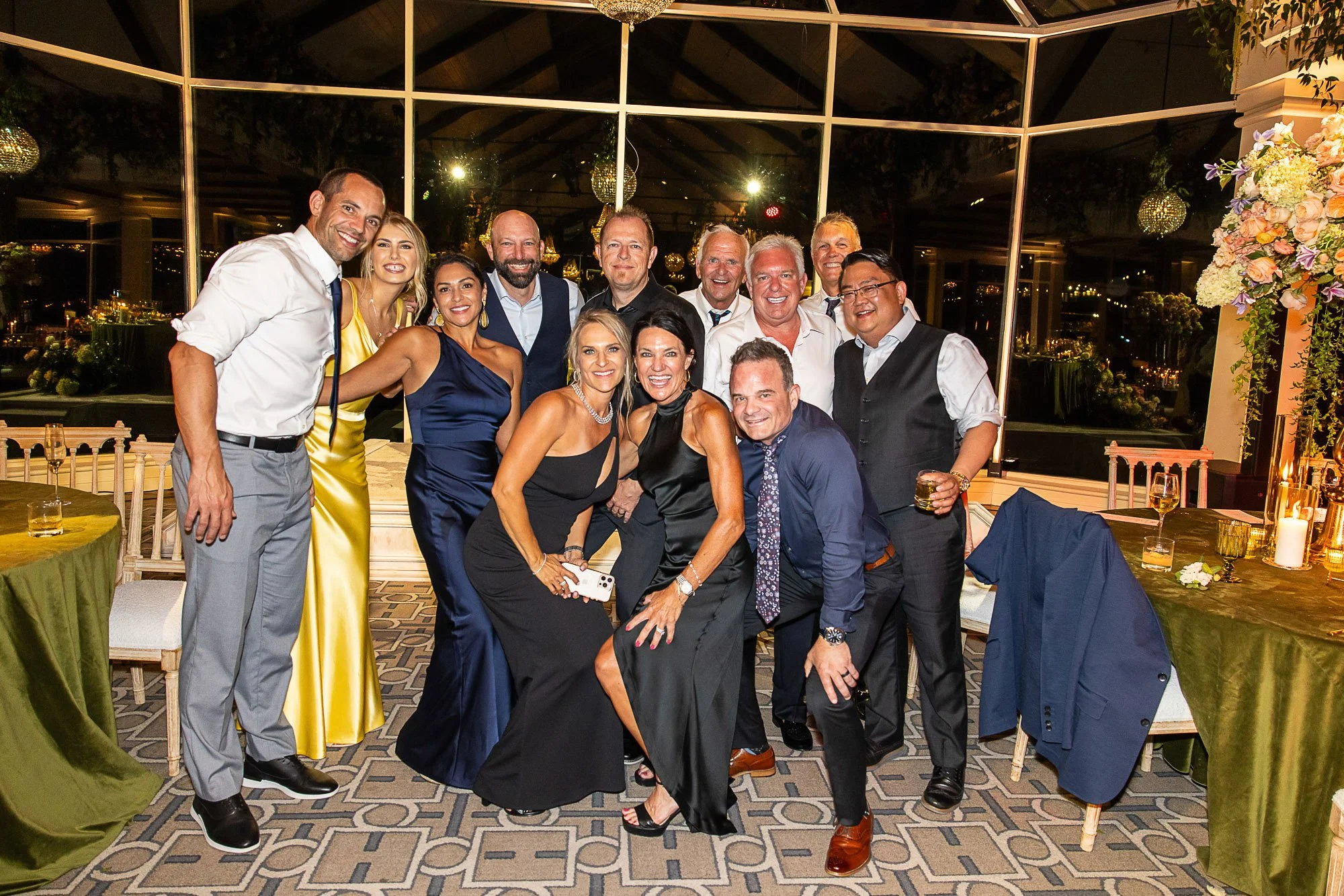 Group of people celebrating at a party or event inside a decorated venue, with some dressed in formal attire, smiling for the camera at the Beach and Tennis Club in Pebble Beach, CA.