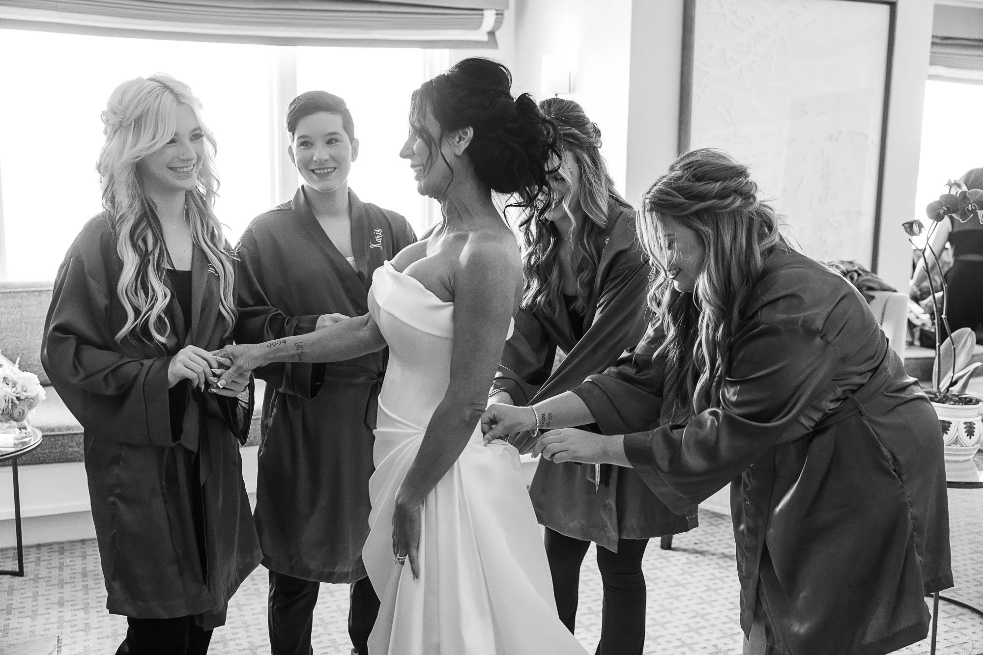 Women helping bride prepare for wedding in a room with natural light at the Beach and Tennis Club in Pebble Beach, CA.
