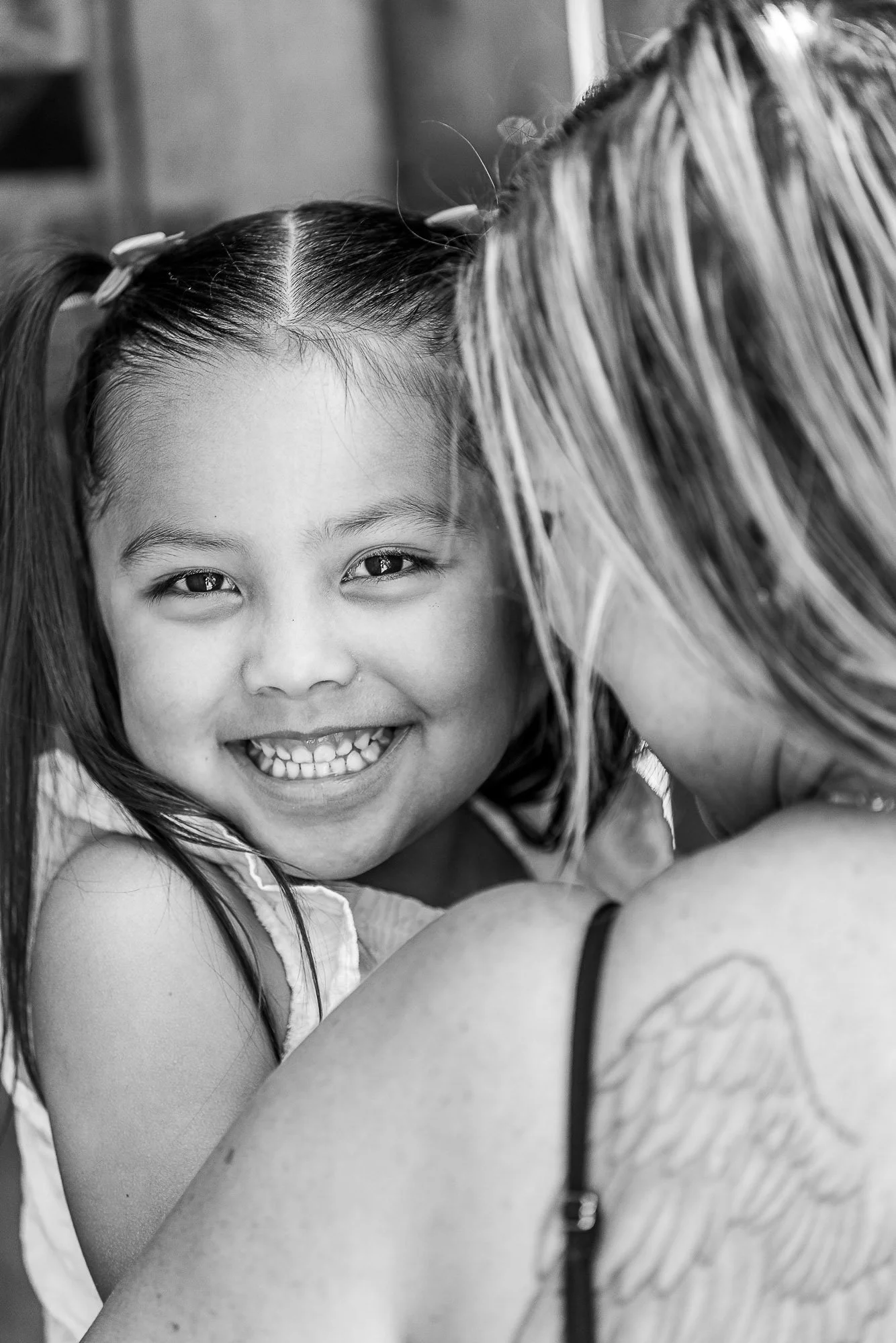 A young girl is smiling widely while hugging someone, with her face close to that person's shoulder, in a black and white photo.