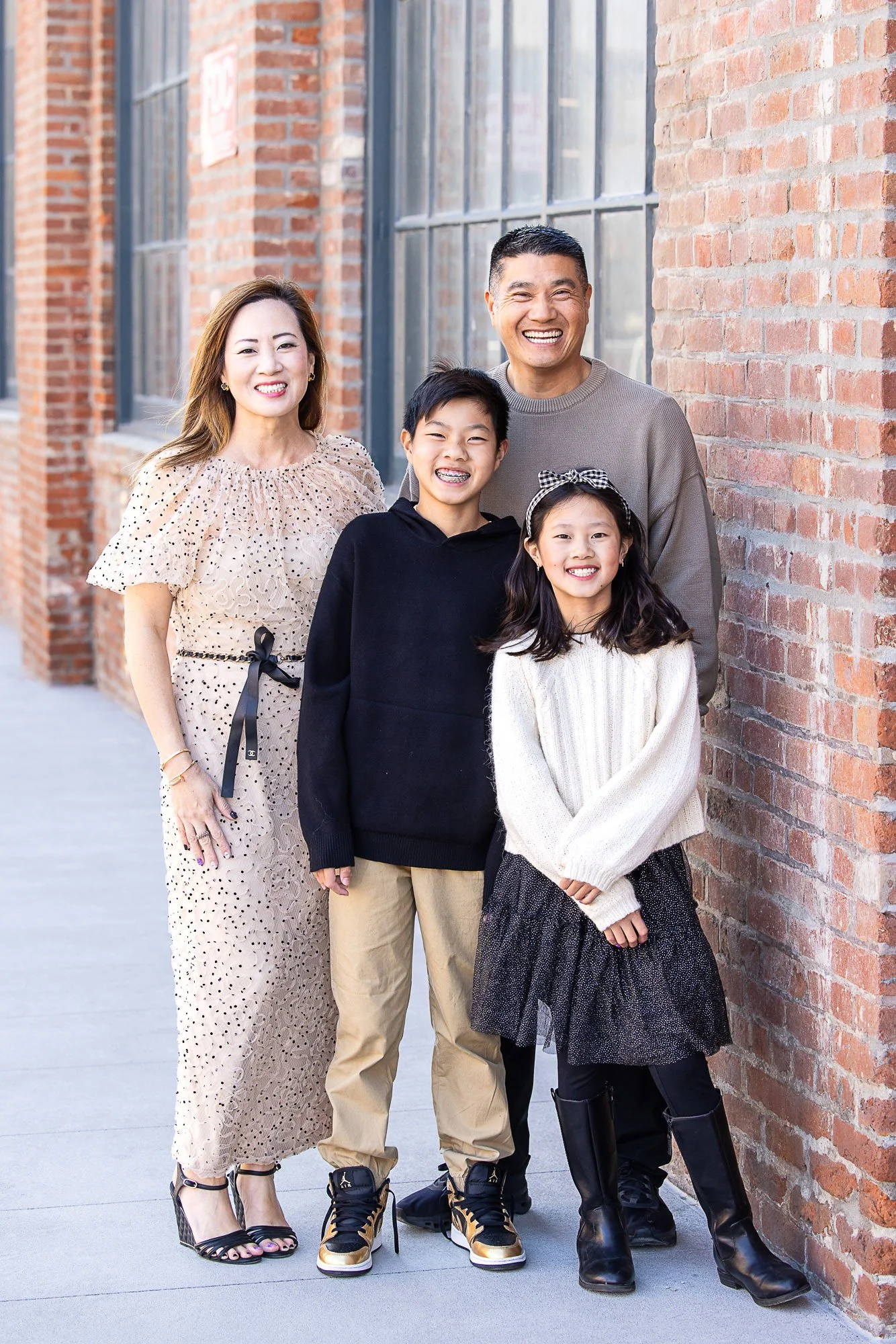 A multi-generational Asian family of five standing outdoors against a brick wall, smiling at the camera.