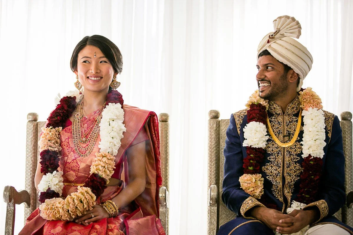 Bride and groom in floral garlands seated during their multicultural wedding ceremony at The Ritz-Carlton, San Francisco