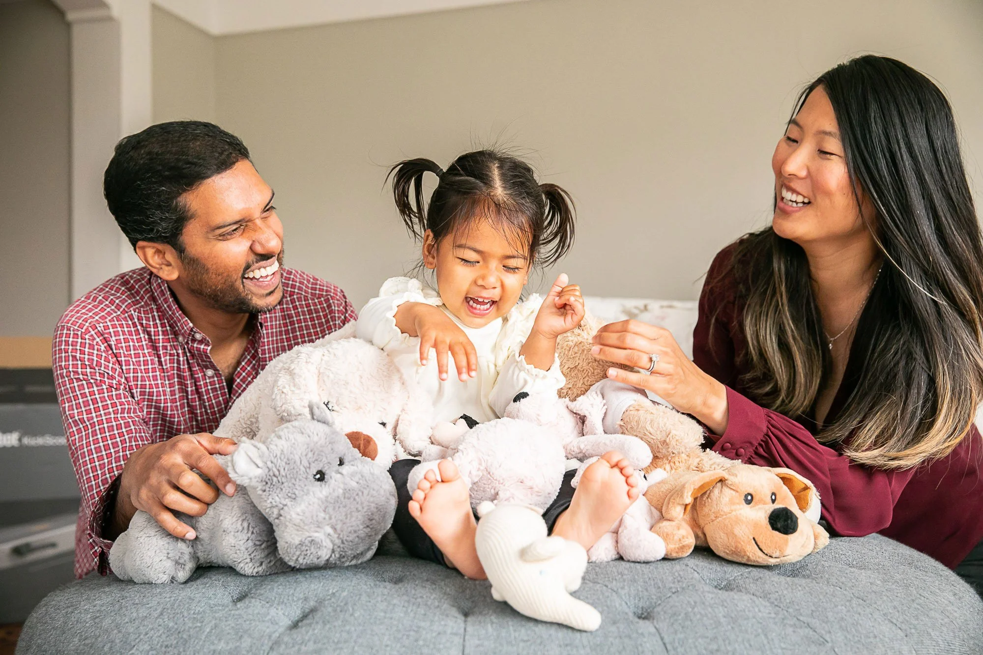 Parents playing with their daughter and her stuffed animals on a bed at home