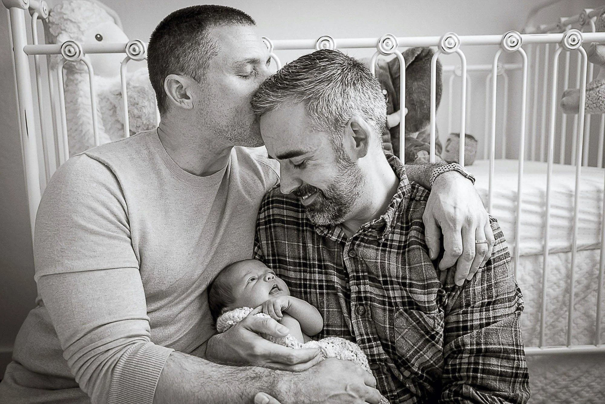 Two fathers with their newborn in the nursery, black and white