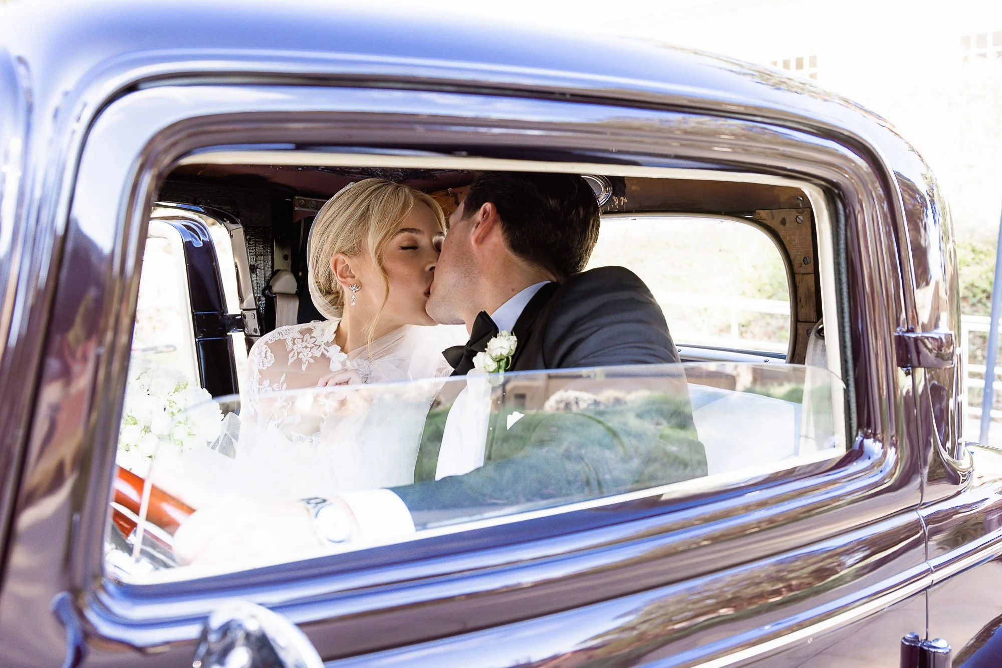 A couple in wedding attire sharing a kiss inside a vintage car at Cavallo Point in Sausalito, CA.