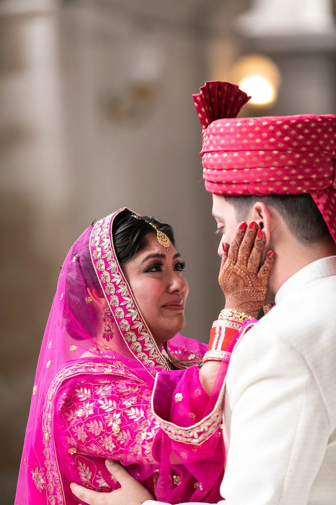 A bride and groom in traditional Indian attire sharing an intimate moment, with the bride touching the groom's face.