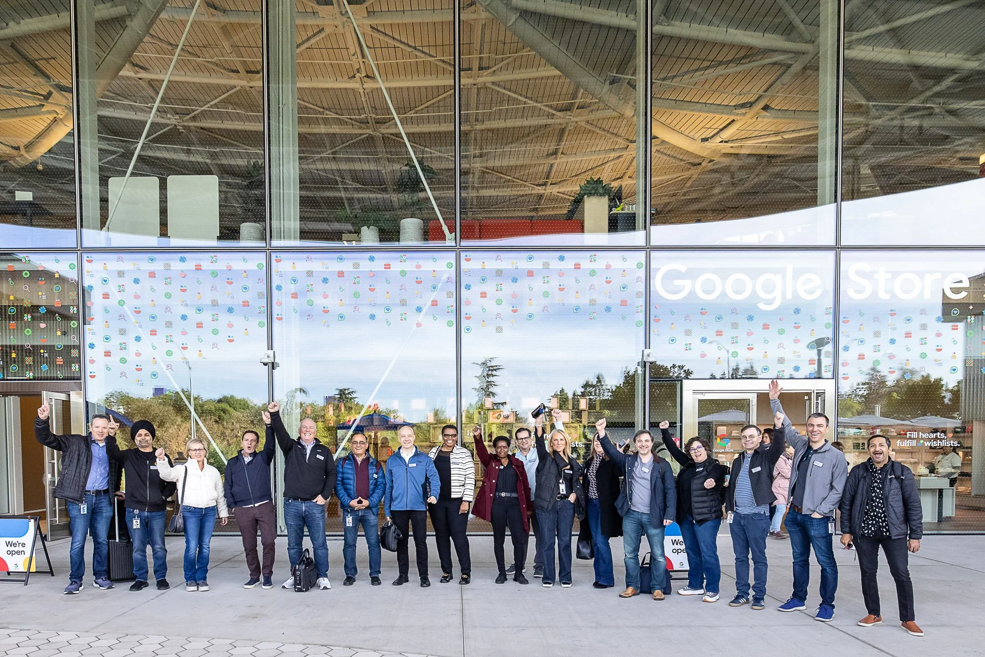 Group of diverse people standing outside Google Store, smiling, and raising their hands in a celebratory manner.